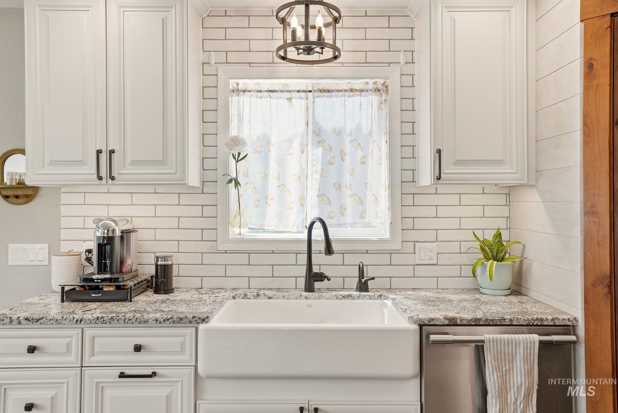 Kitchen features a white farmhouse sink with a matte black gooseneck faucet, light-colored granite-style countertops, white shaker-style cabinetry with dark hardware, a white subway tile backsplash, and a built-in stainless steel dishwasher