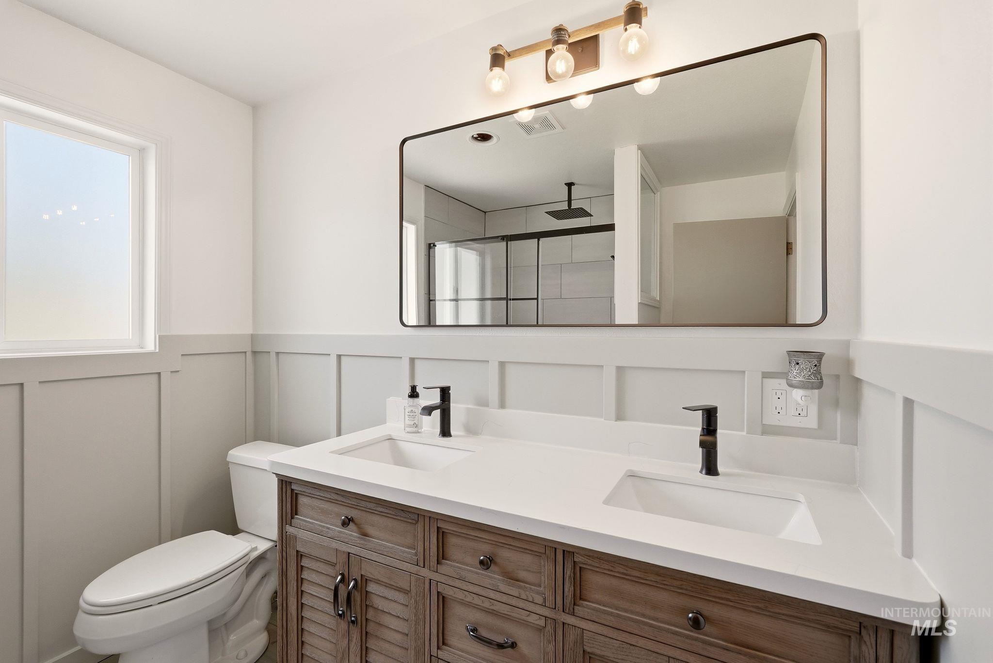 Bathroom featuring a double vanity with stone countertops, a wood-finish cabinet, and matte black fixtures