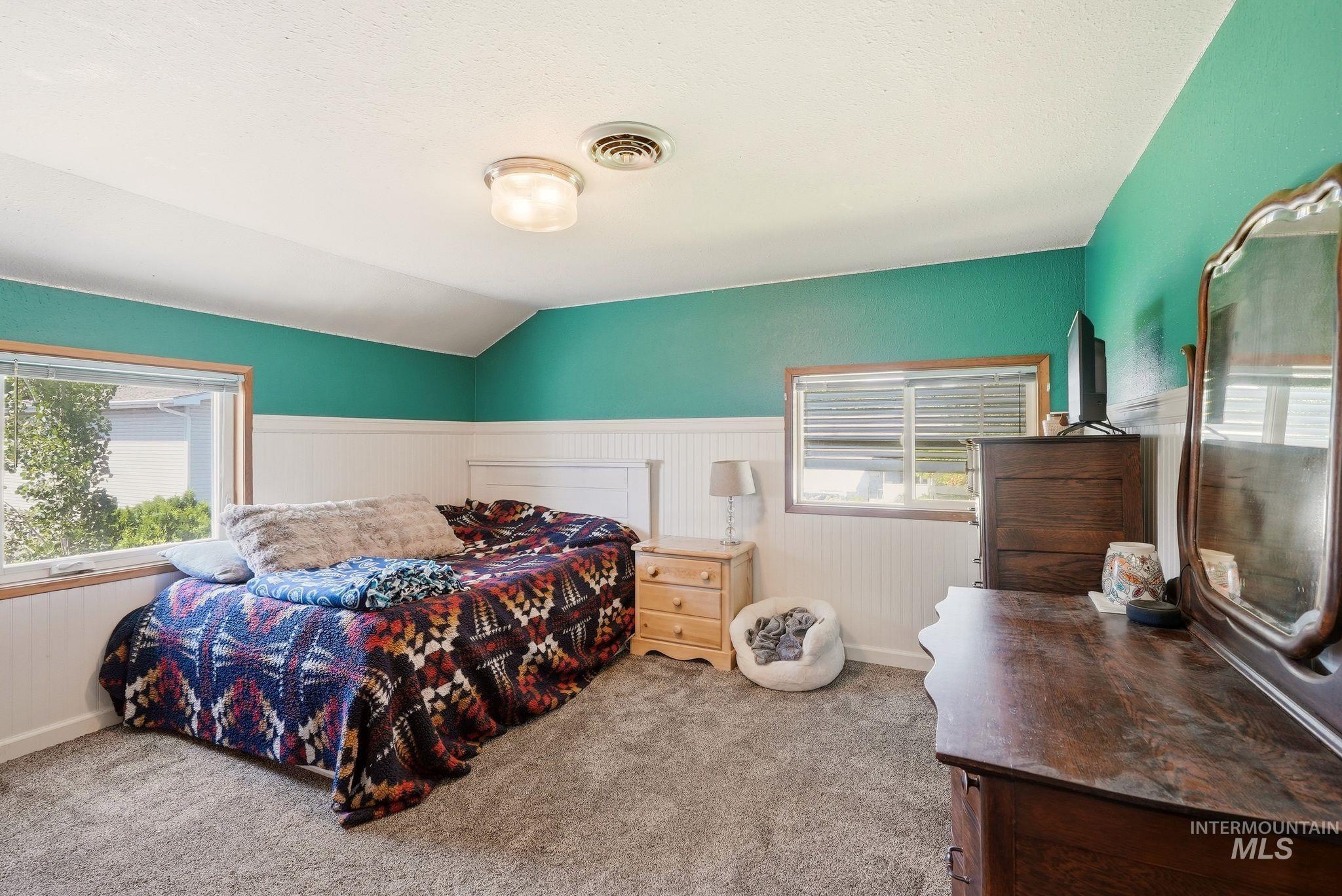 Bedroom with light green painted walls, white wainscoting, and grey carpeting