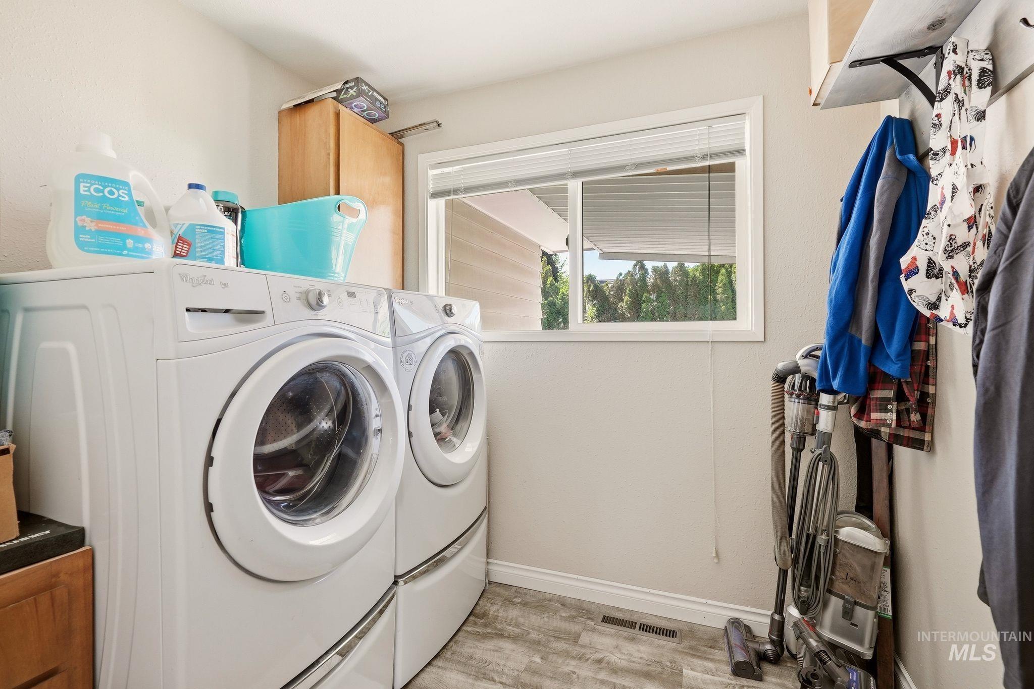 Dedicated laundry area featuring front-loading appliances, wood-finish flooring, a white window with blinds, and light-toned walls