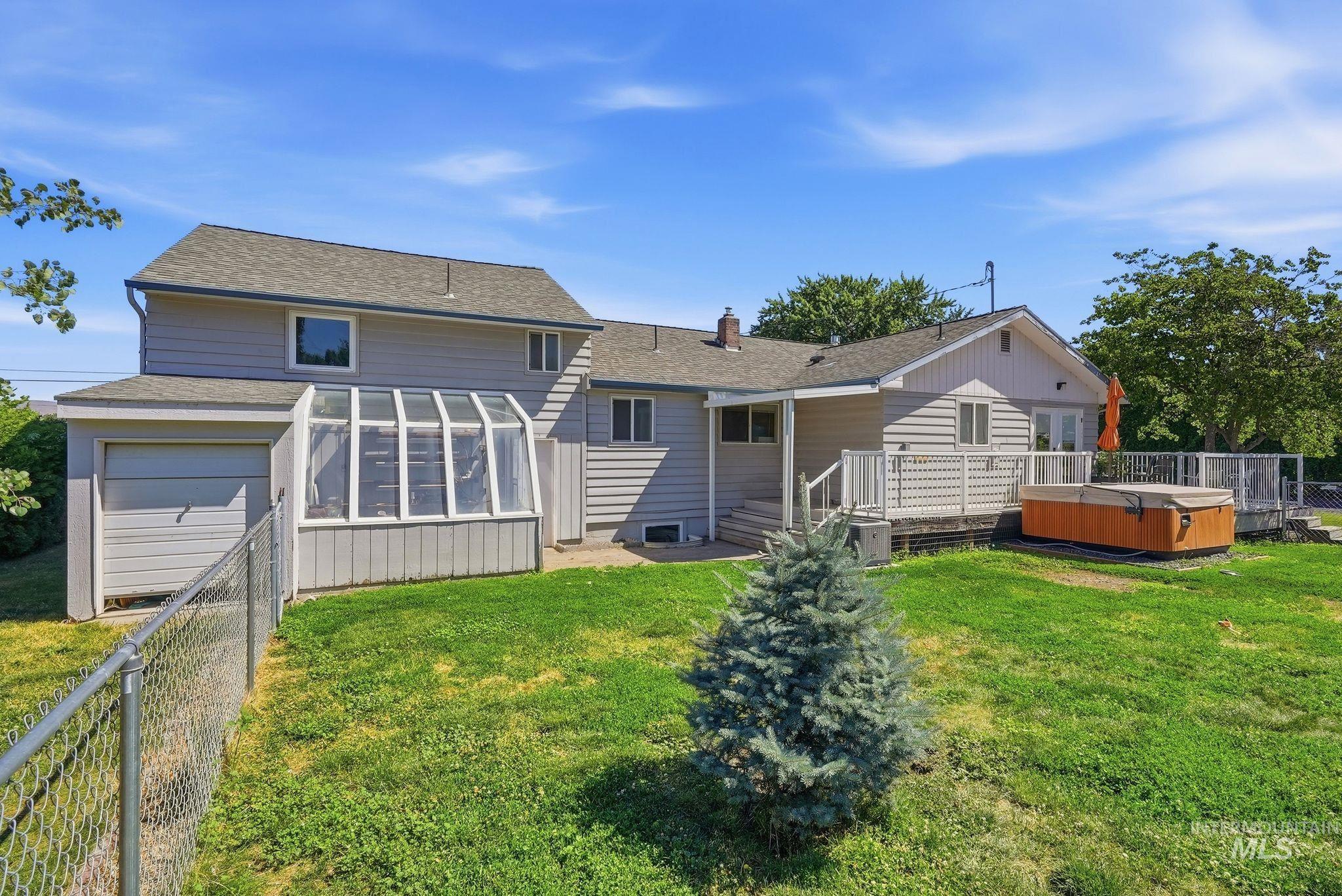 Expansive rear exterior featuring a multi-level deck, built-in hot tub, and an attached sunroom with floor-to-ceiling windows