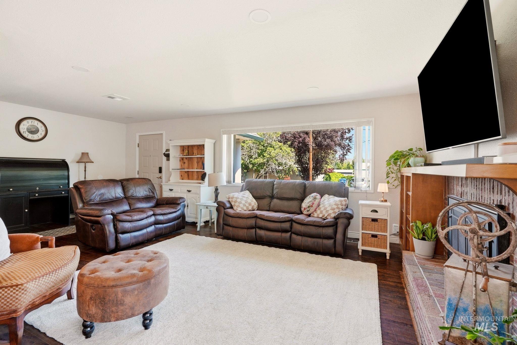 Living area with dark wood-finish flooring, white walls, and a large window providing natural light