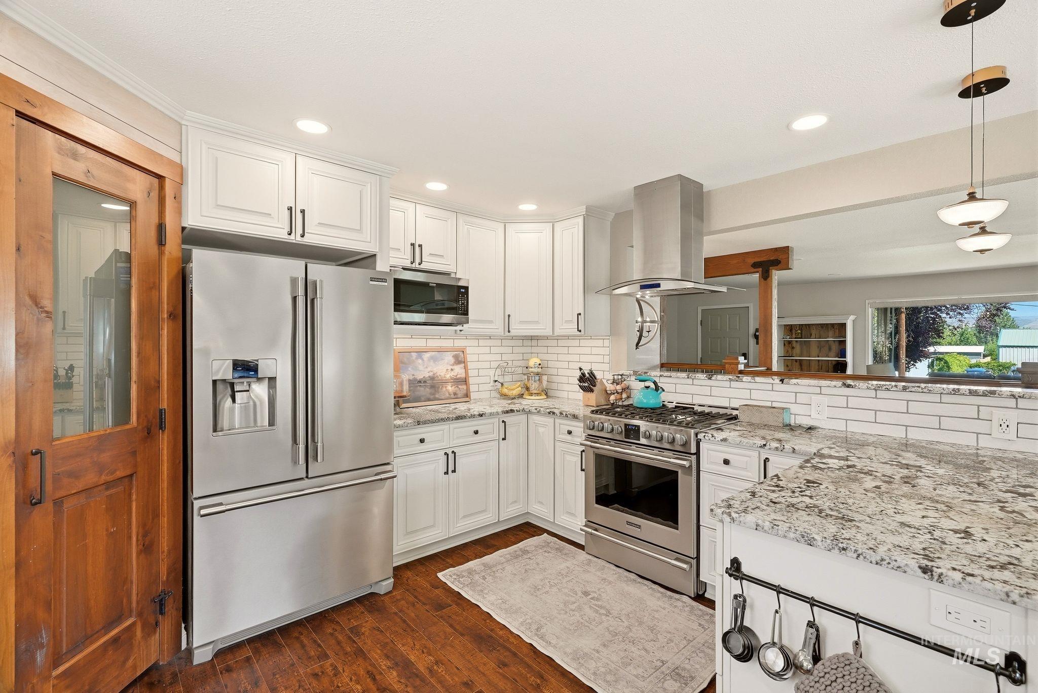 Modern kitchen featuring wood-finish flooring, white cabinetry, stainless steel appliances, and granite-style countertops with a subway tile backsplash