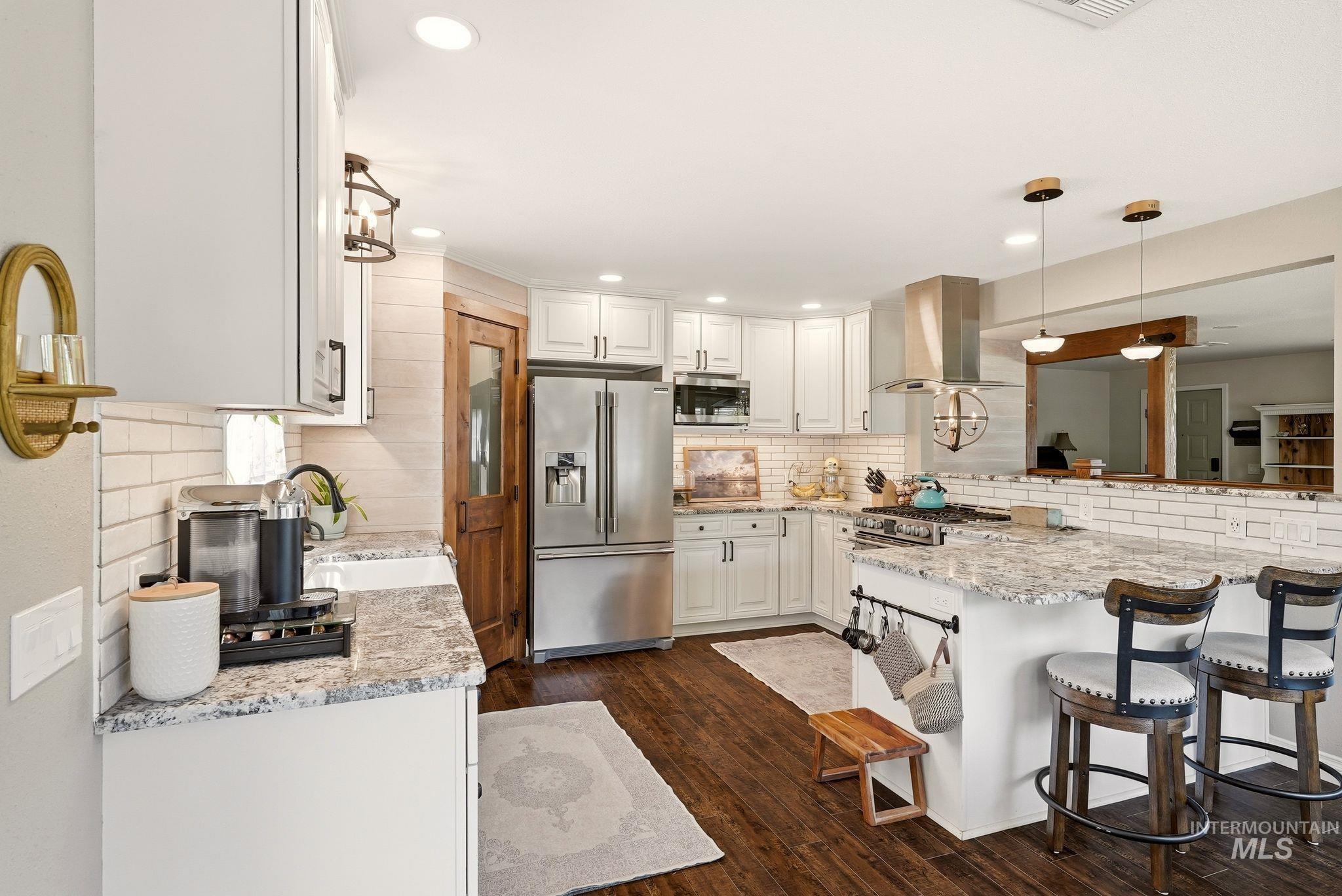 Modern kitchen featuring granite countertops, white cabinetry, stainless steel appliances, a subway tile backsplash, and wood-finish flooring