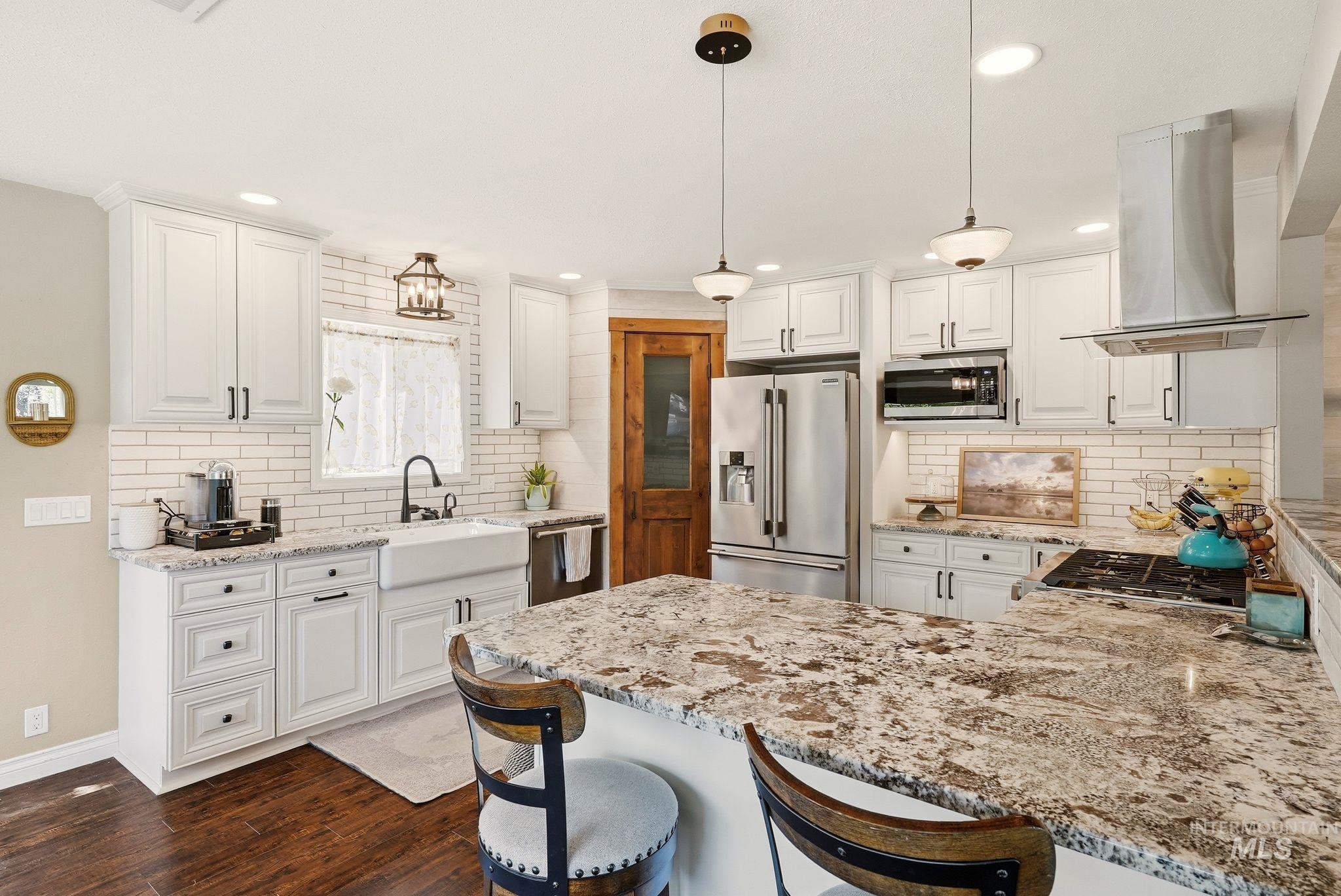 Kitchen featuring white cabinetry, subway tile backsplash, a farmhouse sink, stainless steel appliances, and a central island with a speckled countertop