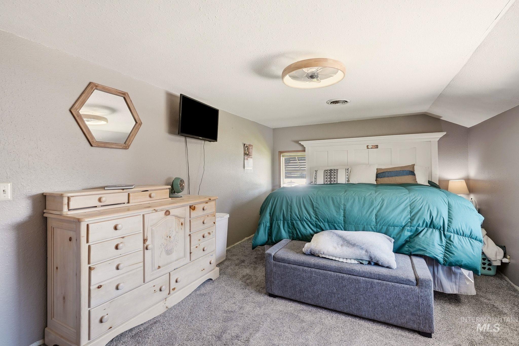 Carpeted room with a ceiling-mounted light fixture, a window with horizontal blinds, and a built-in white headboard