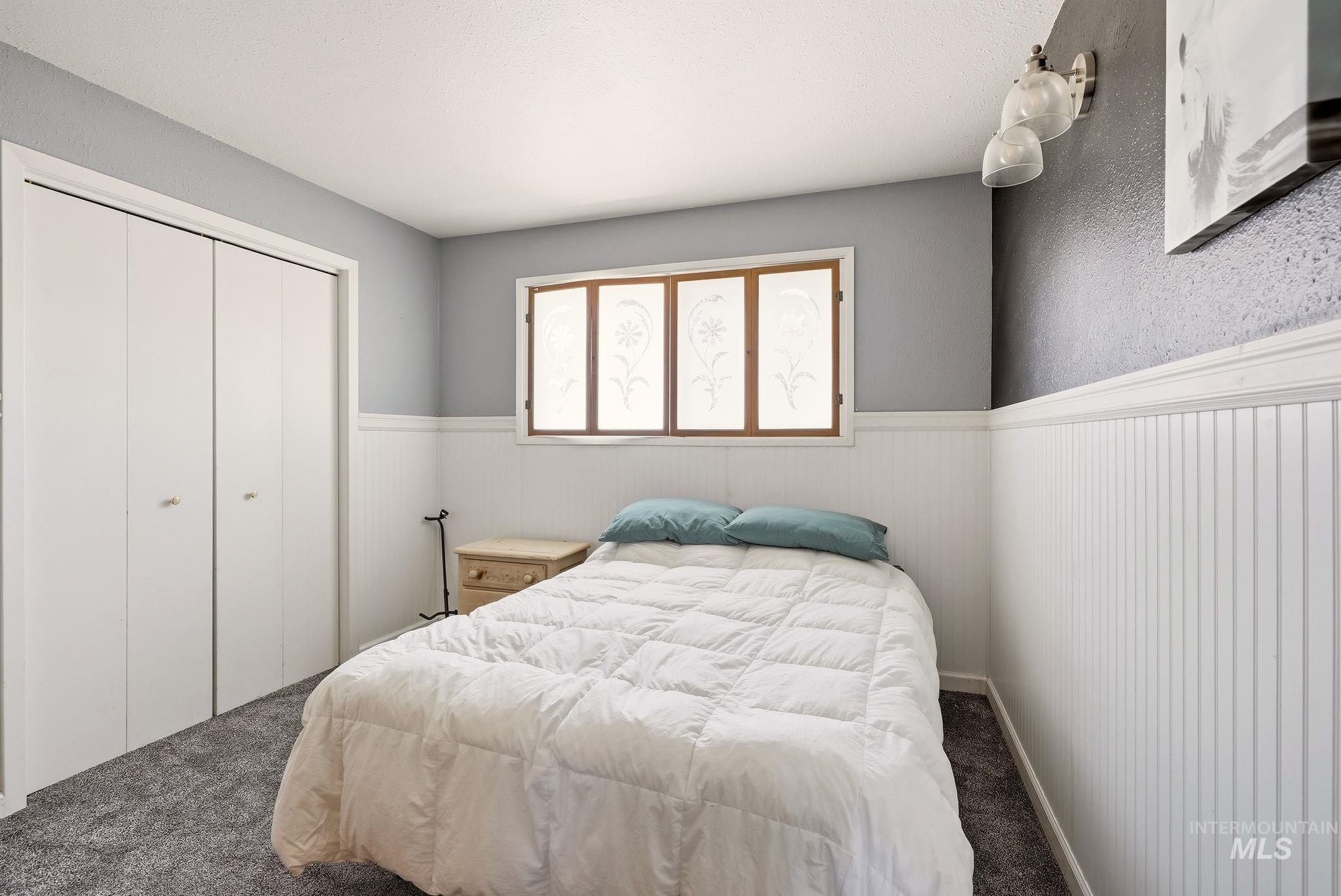 Bedroom featuring a window with decorative glass inserts, white wainscoting, and gray wall paint