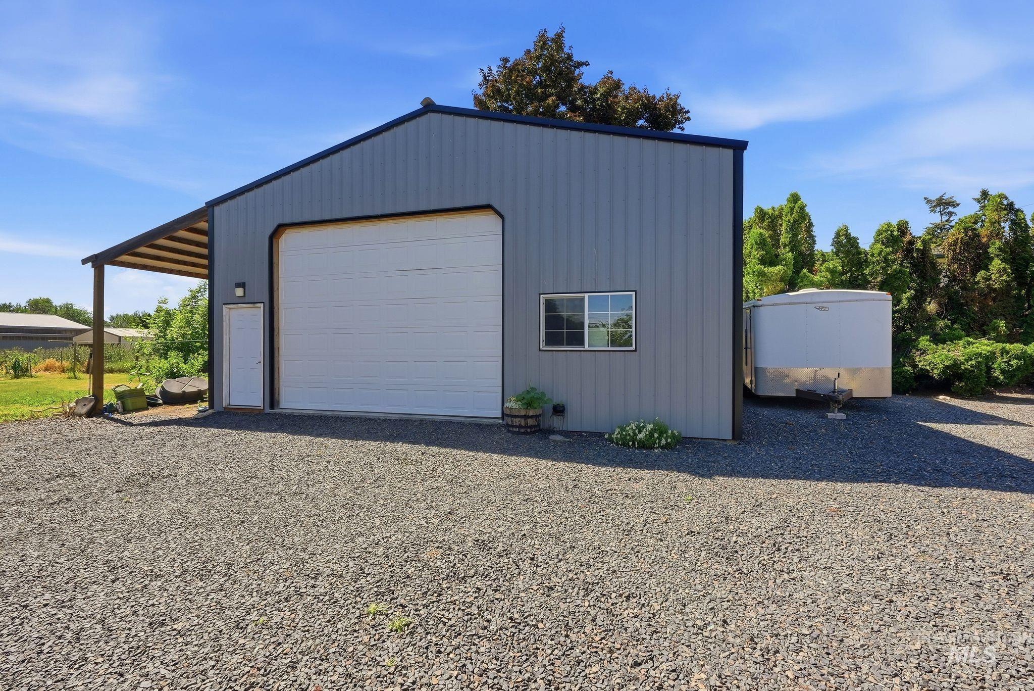 Metal-sided detached garage with a large roll-up door, a dedicated pedestrian door, and an awning-covered side entry