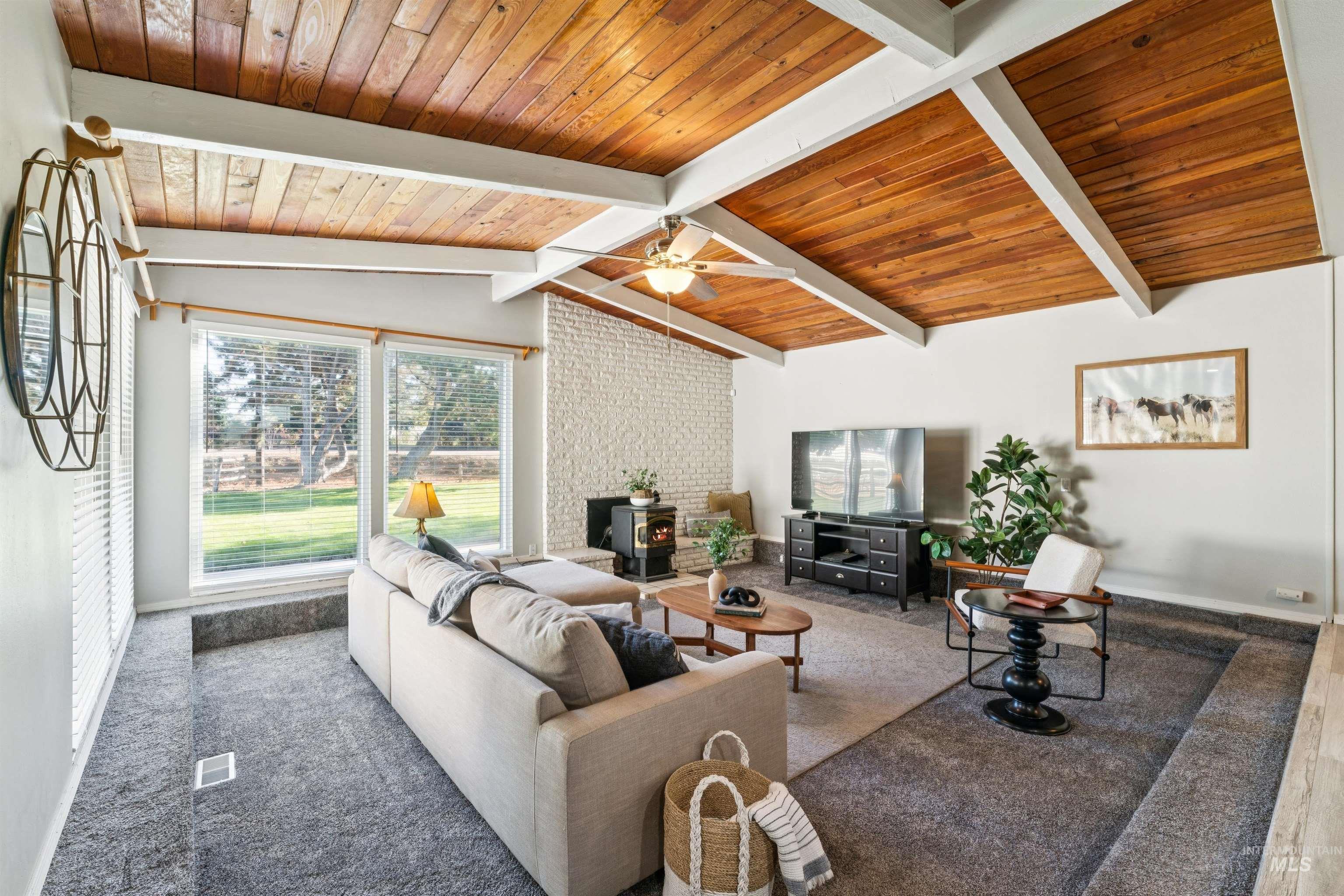 Living room with a wood stove, carpet flooring, wood ceiling, and ceiling fan
