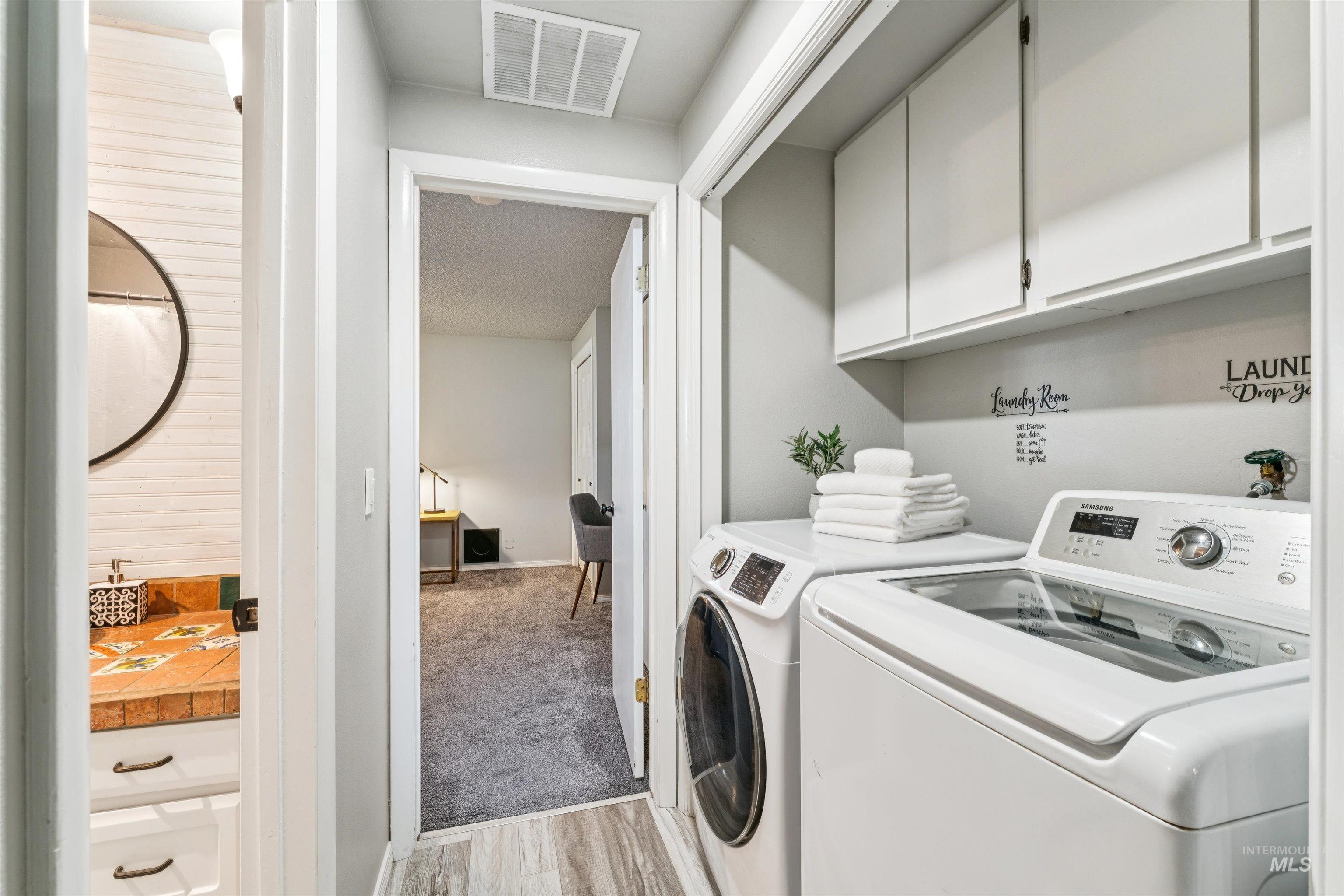 Washroom with light wood-style floors, cabinet space, washing machine and dryer, and light colored carpet