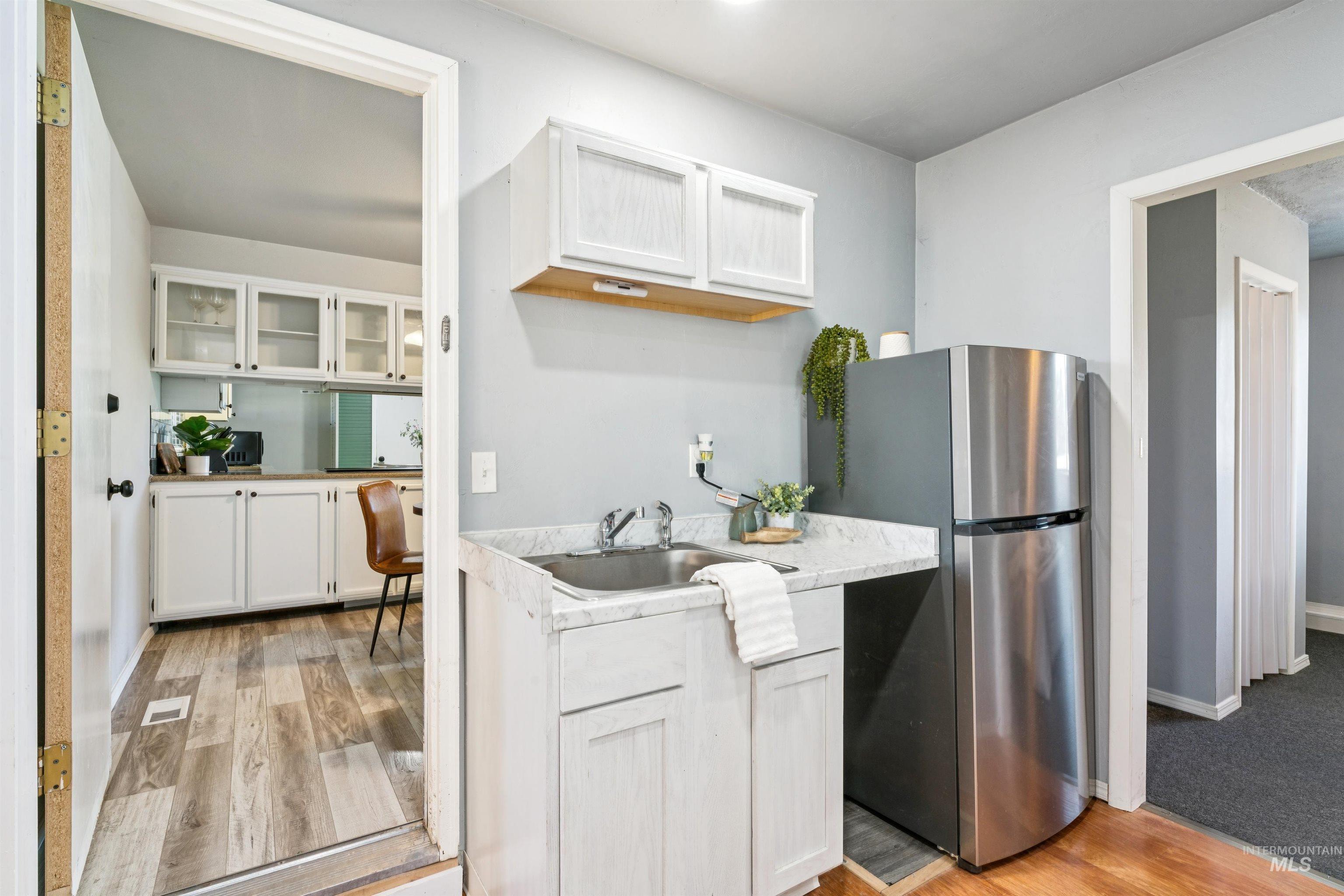 Kitchen with white cabinets, light countertops, freestanding refrigerator, light wood-type flooring, and glass insert cabinets