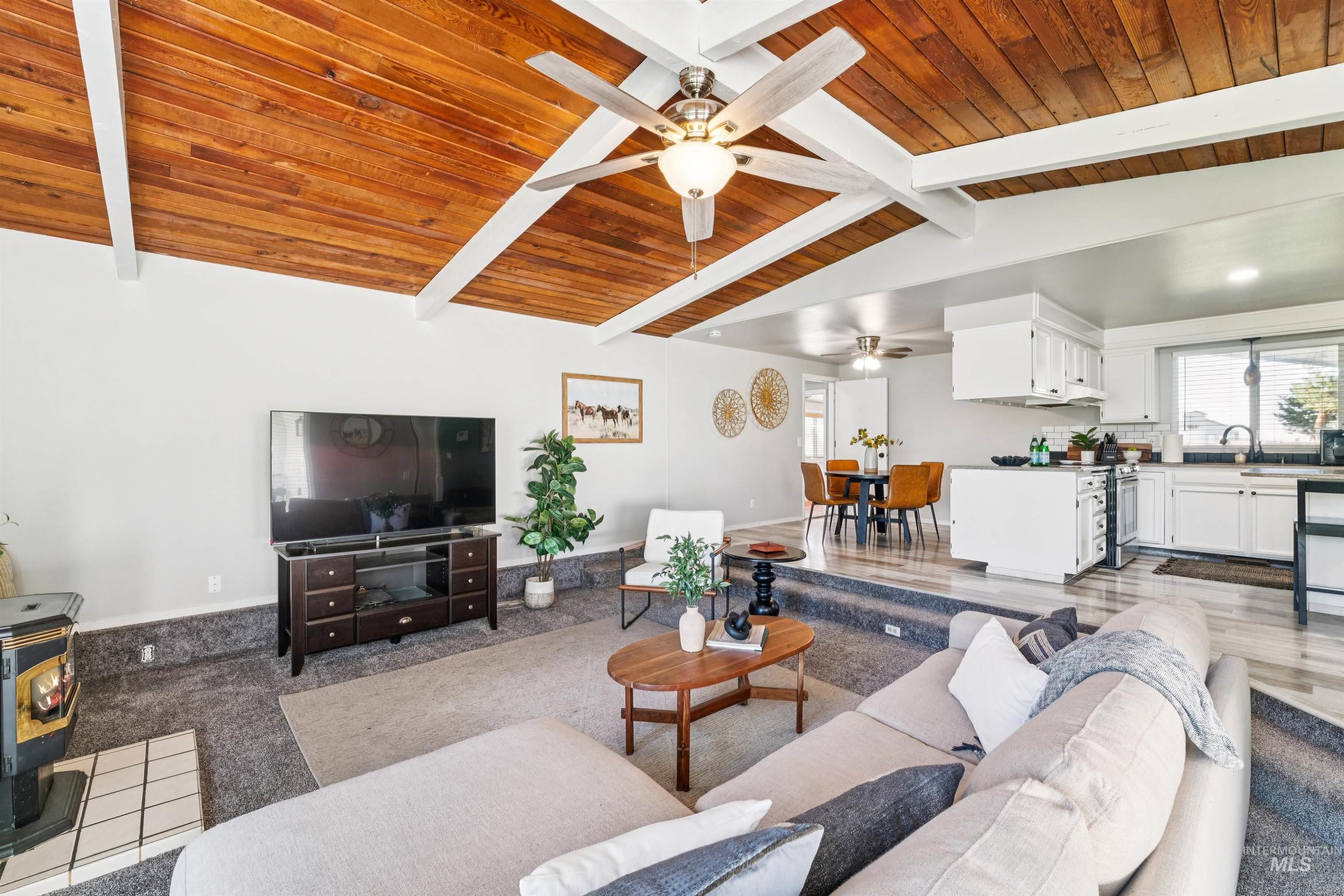 Living area featuring a wood stove, ceiling fan, and wooden ceiling