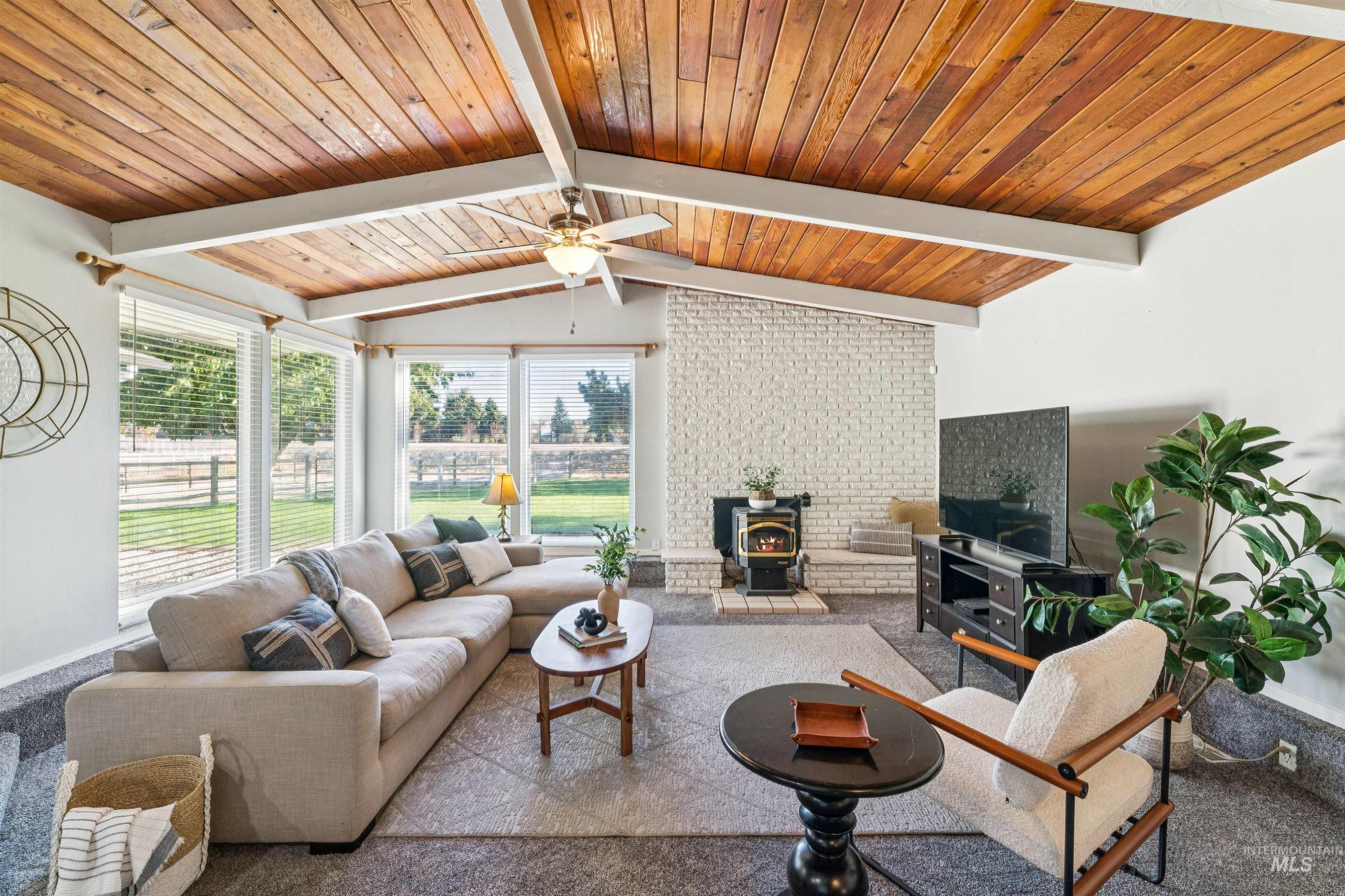 Living area featuring a wood stove, carpet, plenty of natural light, wood ceiling, and ceiling fan