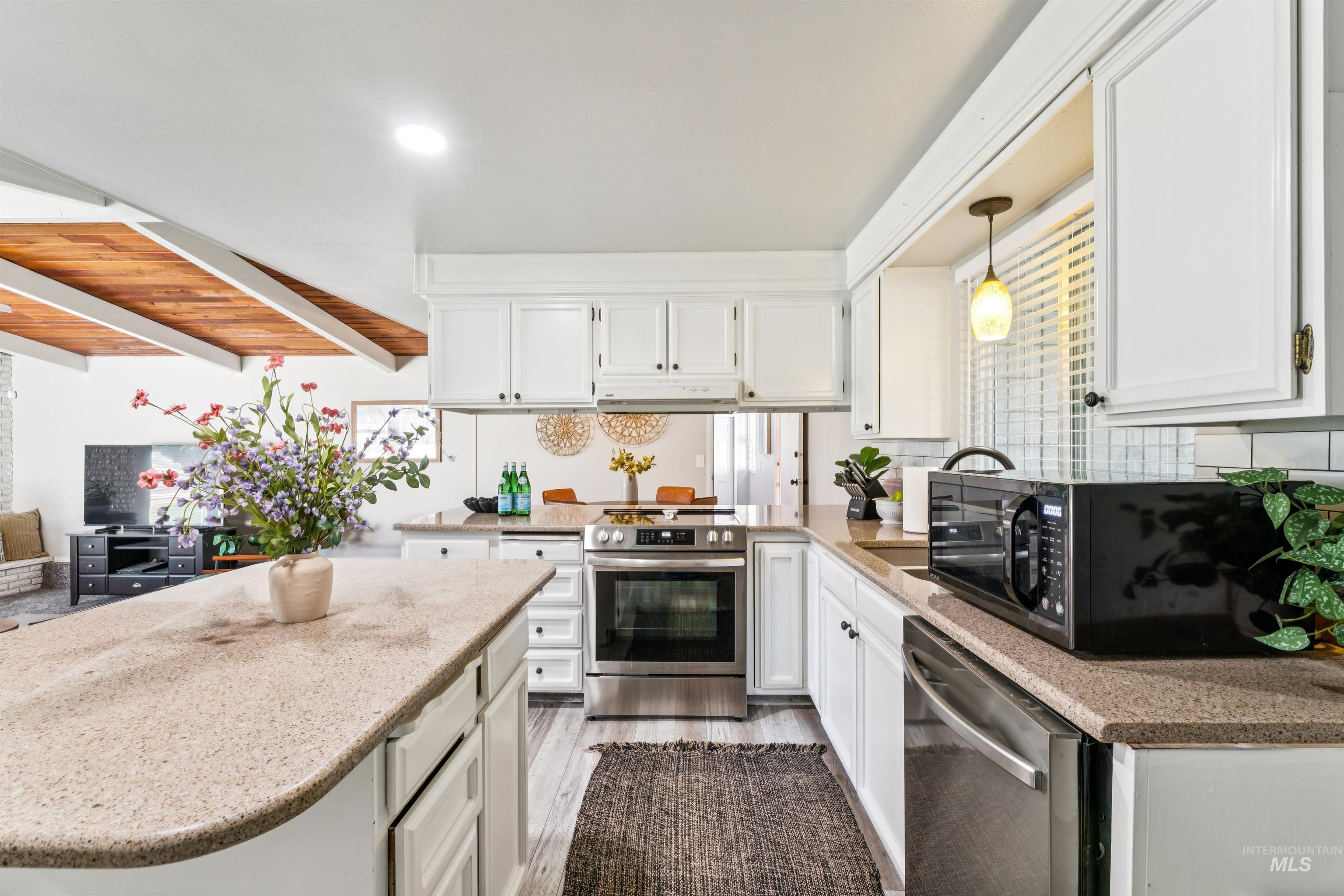 Kitchen featuring white cabinetry, light stone counters, stainless steel appliances, beam ceiling, and light wood-type flooring