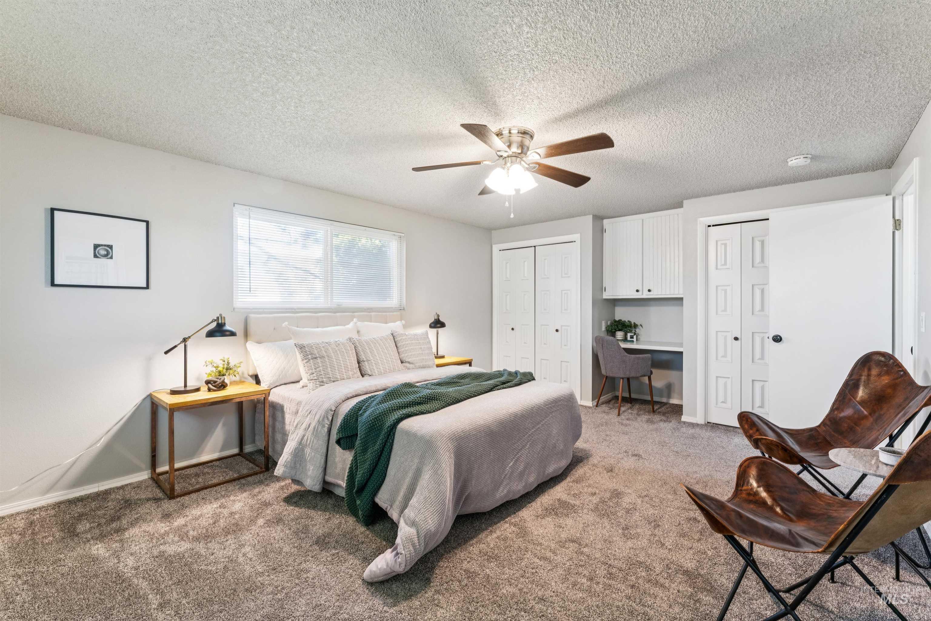 Carpeted bedroom with multiple closets, a ceiling fan, a textured ceiling, and a desk
