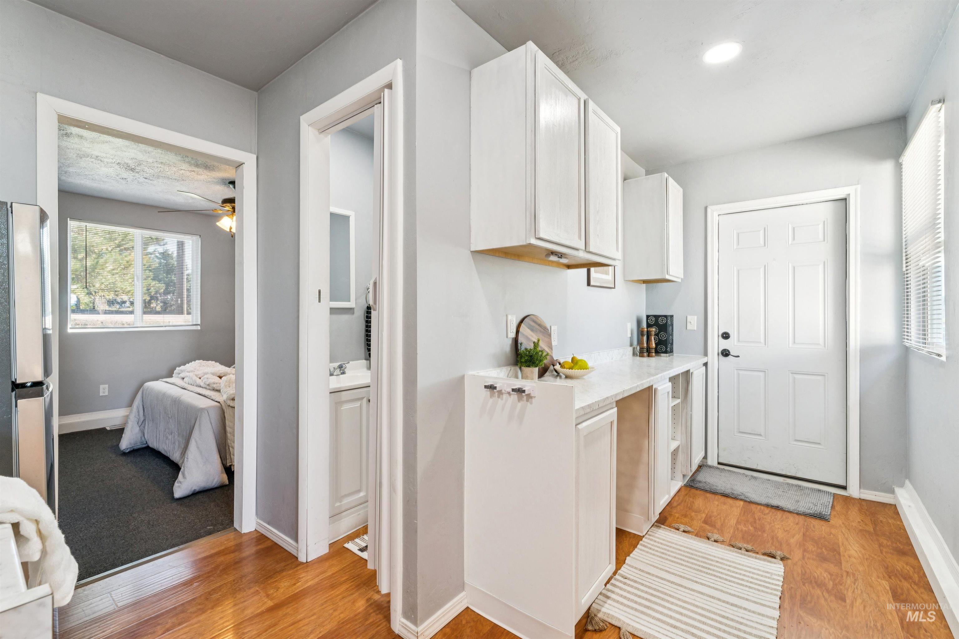 Kitchen featuring light wood finished floors, white cabinetry, freestanding refrigerator, ceiling fan, and light stone countertops