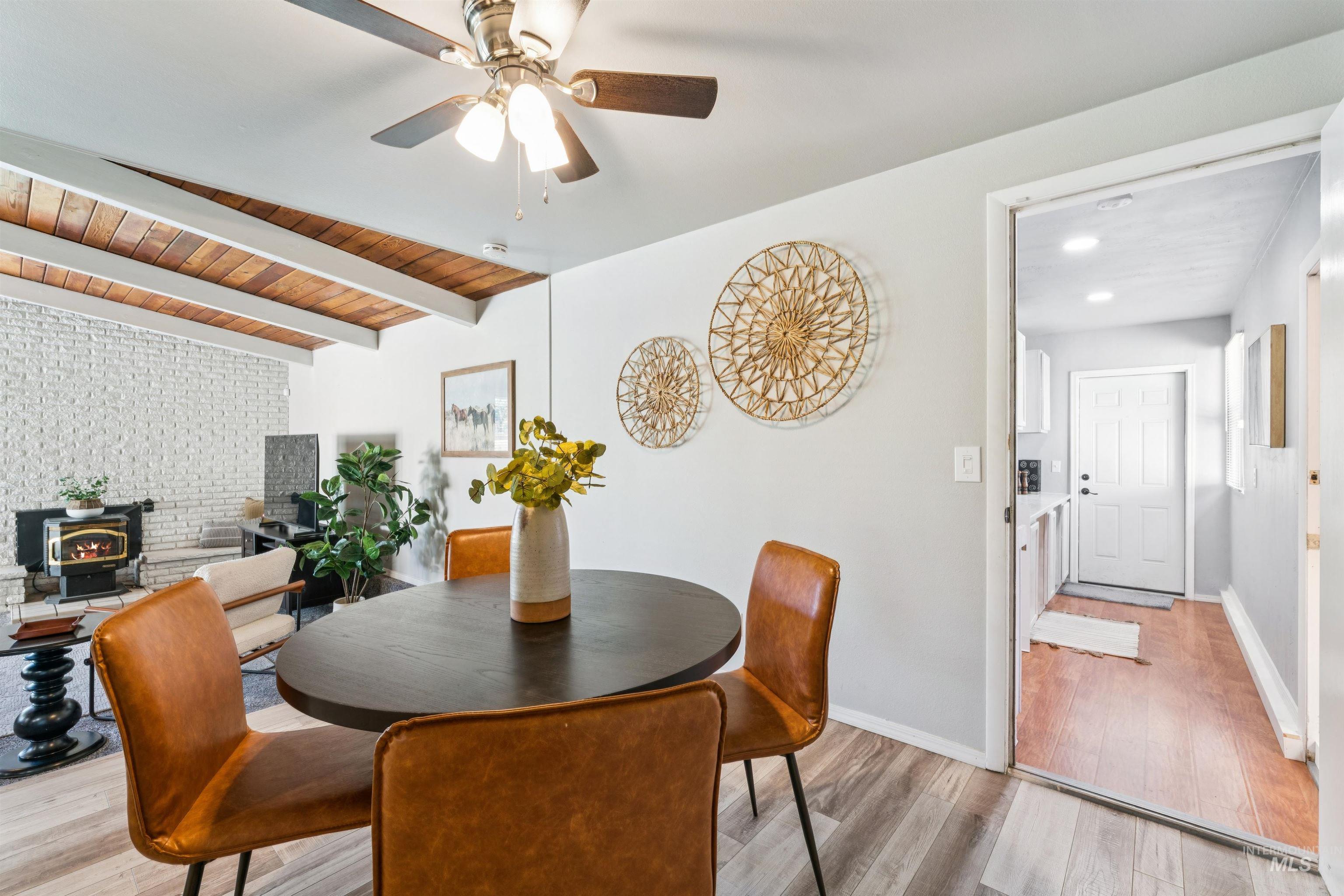 Dining room with a wood stove, light wood-style flooring, a wooden ceiling with exposed beams, and ceiling fan