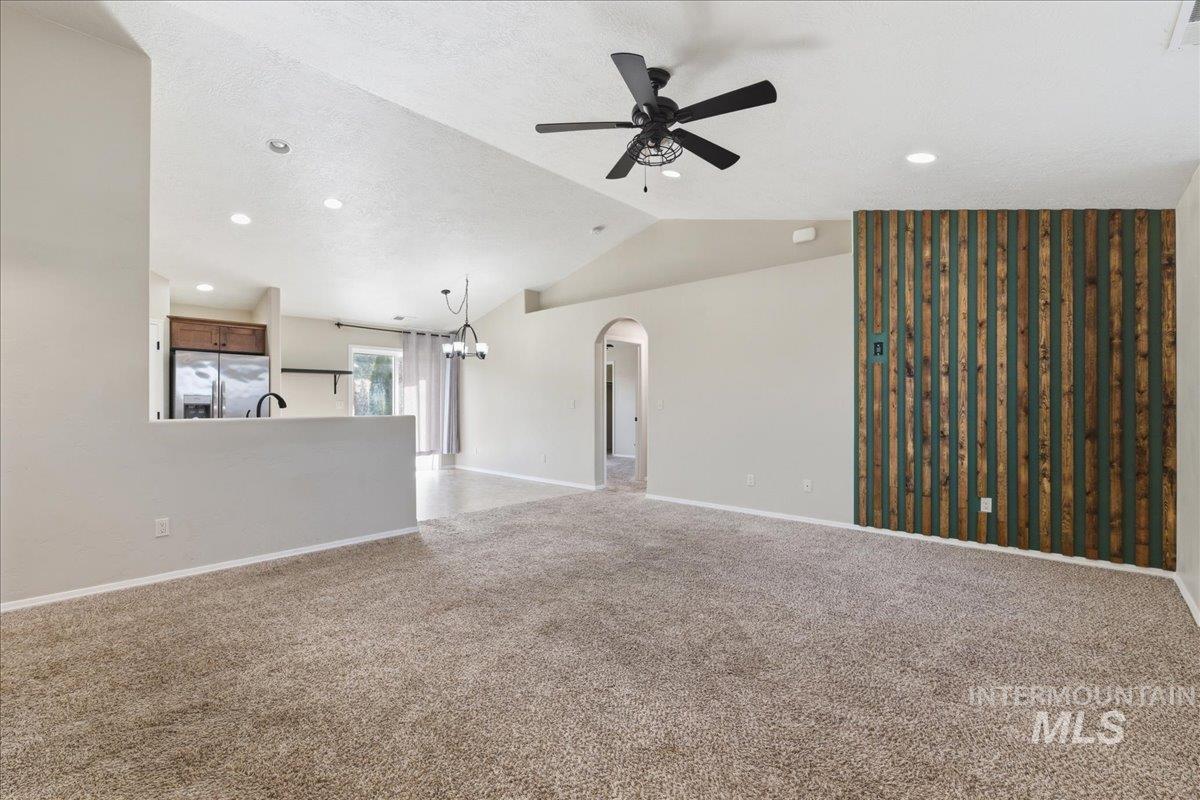 Unfurnished living room with arched walkways, a ceiling fan, light carpet, a chandelier, and a textured ceiling