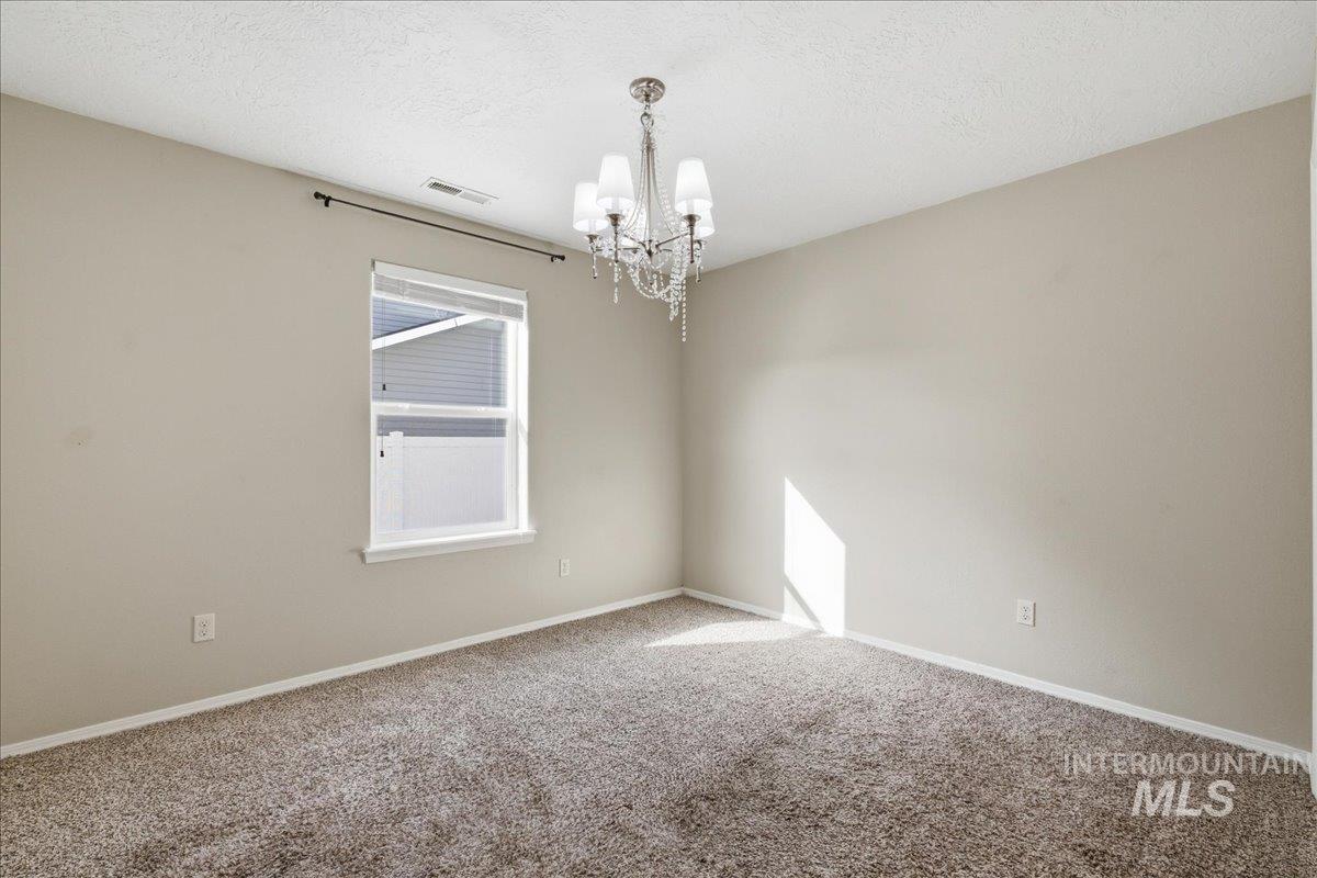 Unfurnished room with hanging lights, carpet flooring, and a textured ceiling