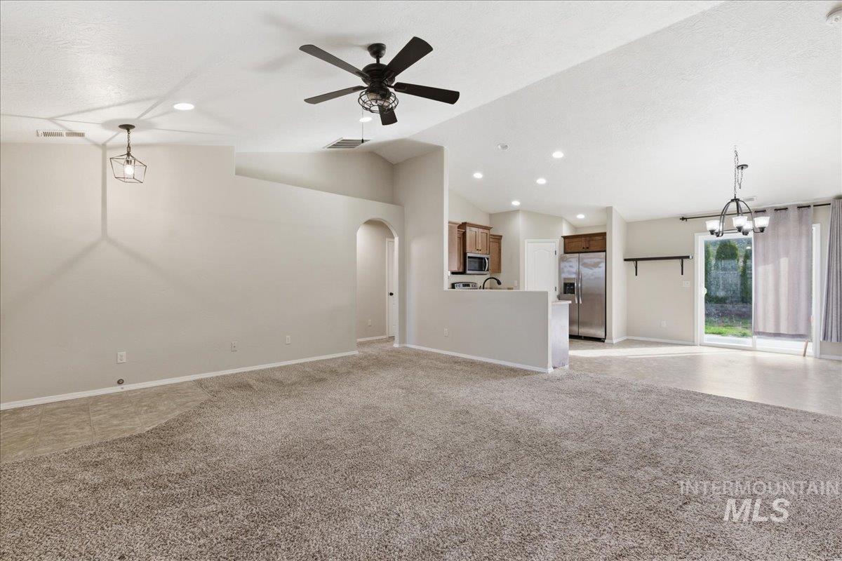 Unfurnished living room with arched walkways, a ceiling fan, light colored carpet, vaulted ceiling, and hanging lights
