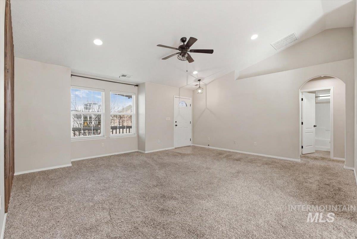 Unfurnished living room with a ceiling fan, light colored carpet, vaulted ceiling, arched walkways, and recessed lighting