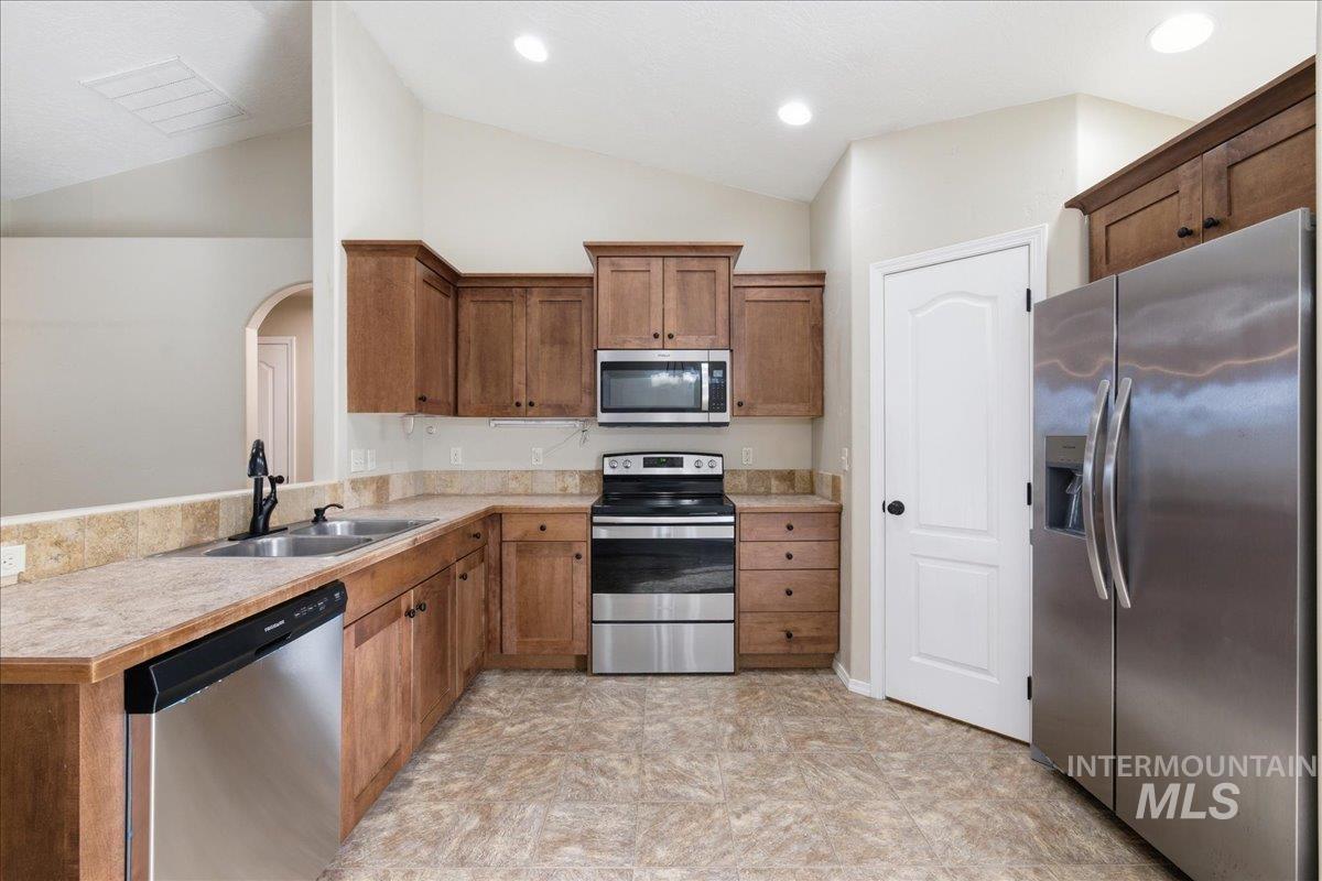 Kitchen featuring stainless steel appliances, light countertops, arched walkways, wood finish cabinets, and vaulted ceiling