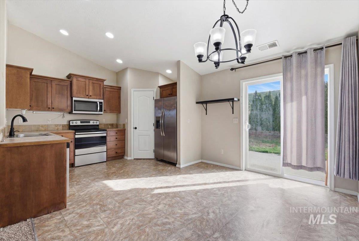Kitchen with stainless steel appliances, light countertops, hanging lights, lofted ceiling, and wood finish cabinets