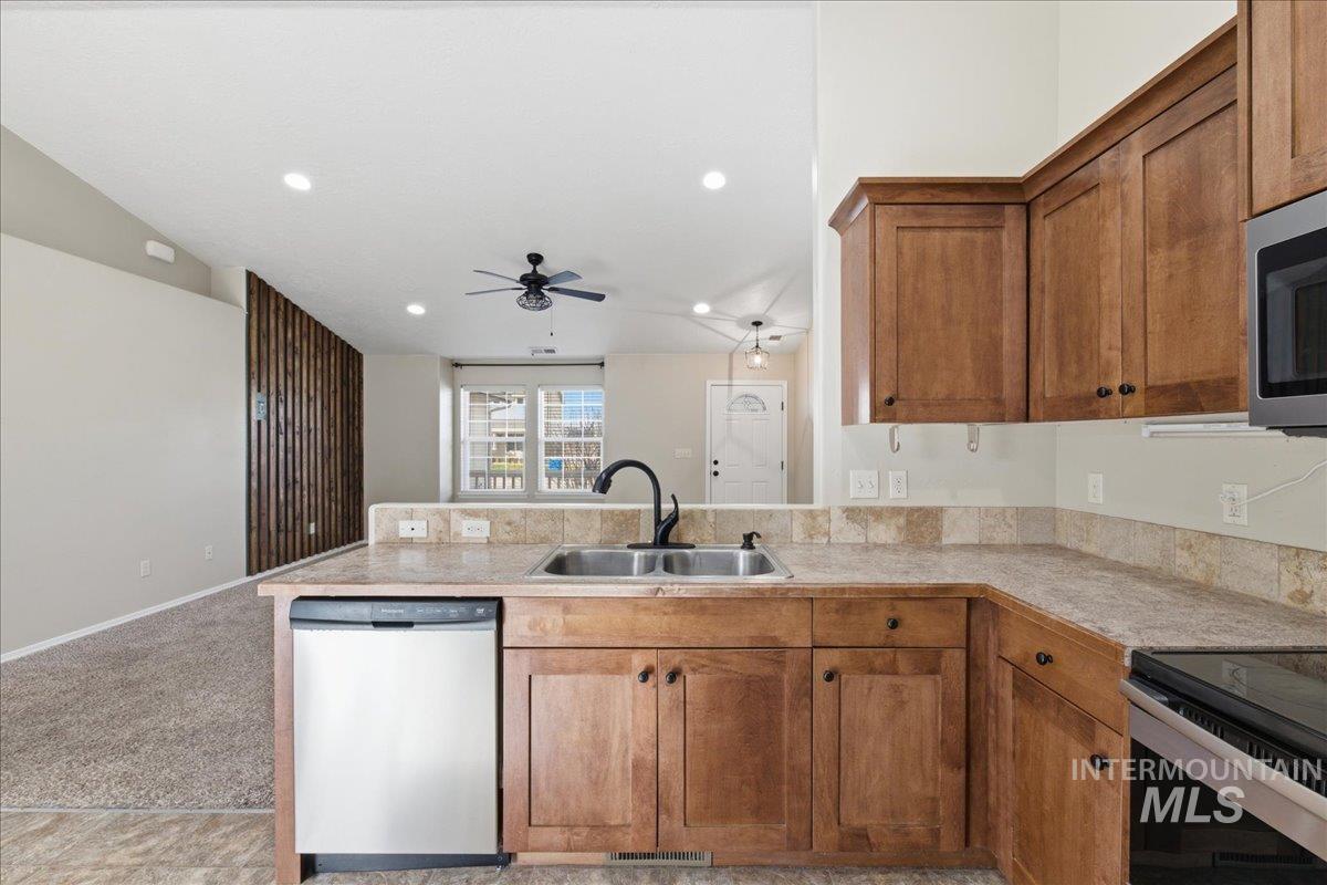 Kitchen featuring stainless steel appliances, light countertops, wood finish cabinets, a peninsula, and light carpet