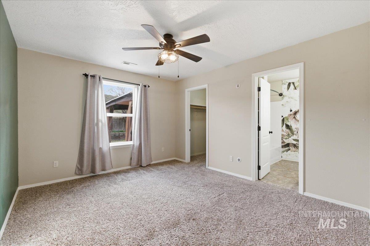 Unfurnished bedroom with a walk in closet, light colored carpet, a ceiling fan, a textured ceiling, and ensuite bathroom