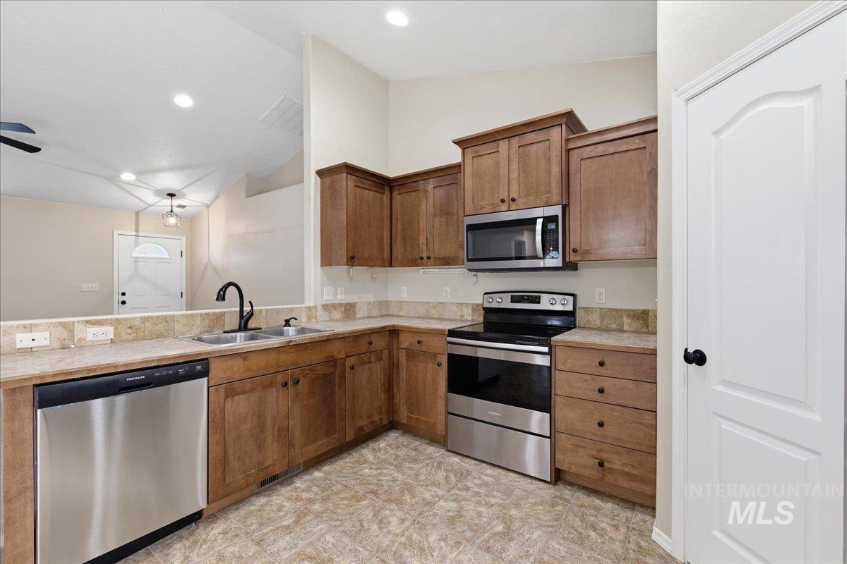 Kitchen featuring stainless steel appliances, light countertops, vaulted ceiling, wood finish cabinetry, and a peninsula