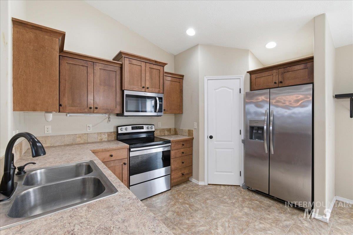 Kitchen featuring stainless steel appliances, light countertops, vaulted ceiling, and recessed lighting