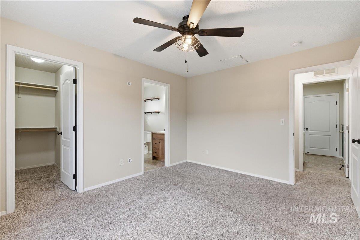 Unfurnished bedroom featuring a walk in closet, light colored carpet, a ceiling fan, and connected bathroom