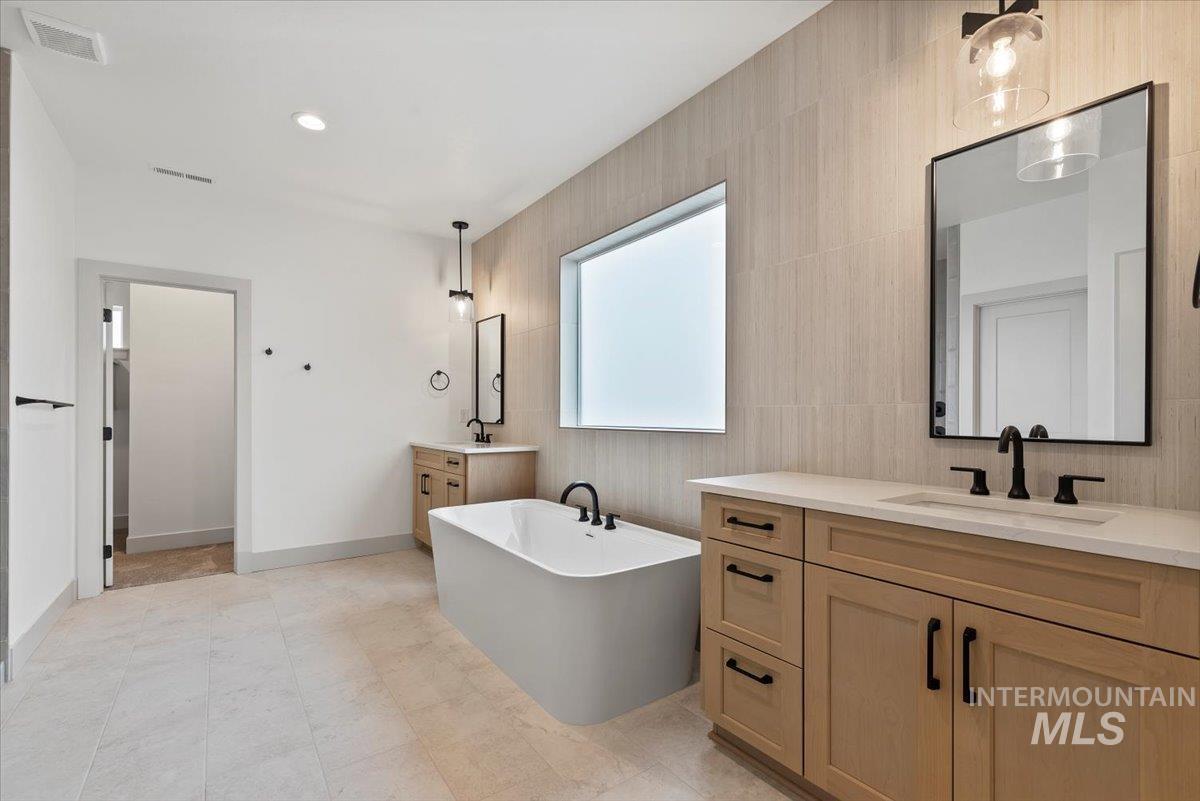 Full bath featuring a freestanding bath, two vanities, tile walls, and recessed lighting