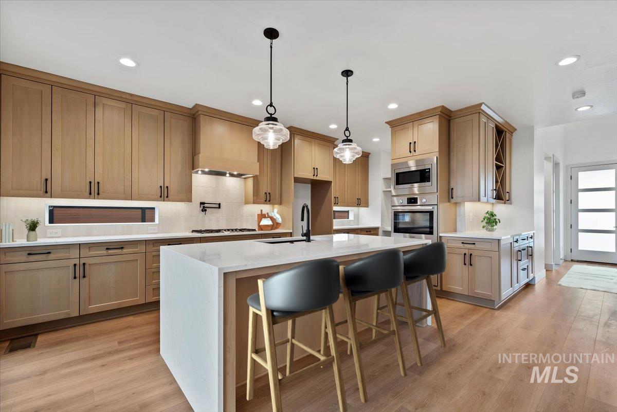 Kitchen featuring a kitchen bar, light stone countertops, decorative light fixtures, light wood-style flooring, and backsplash