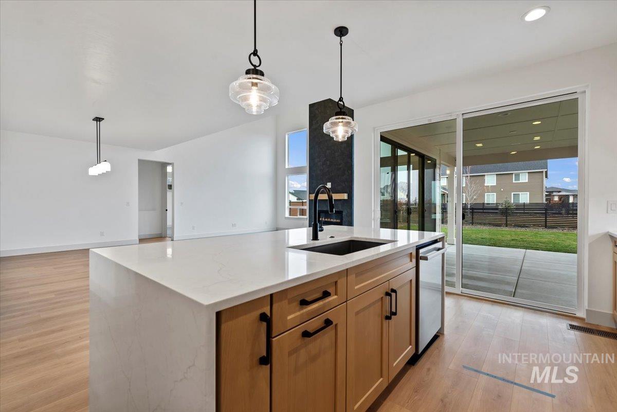 Kitchen with light wood finished floors, decorative light fixtures, an island with sink, and open floor plan