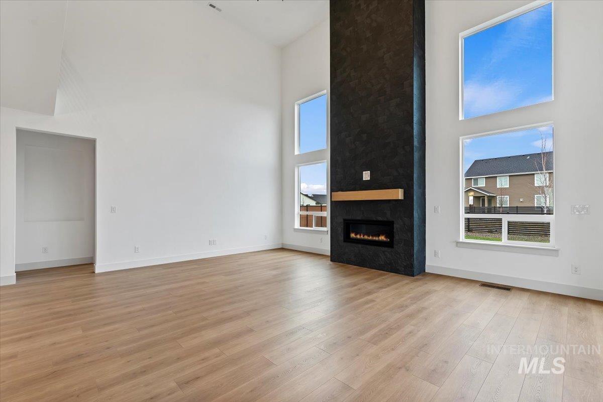 Unfurnished living room featuring a towering ceiling, a large fireplace, and light wood-type flooring