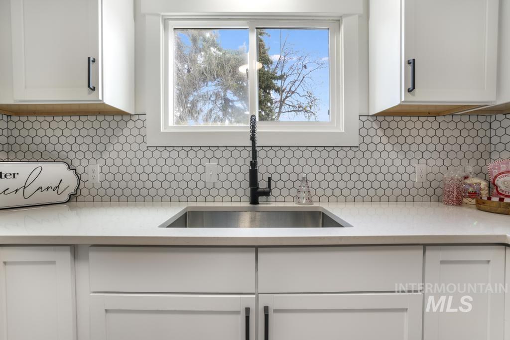 Kitchen featuring light stone counters, backsplash, and white cabinets