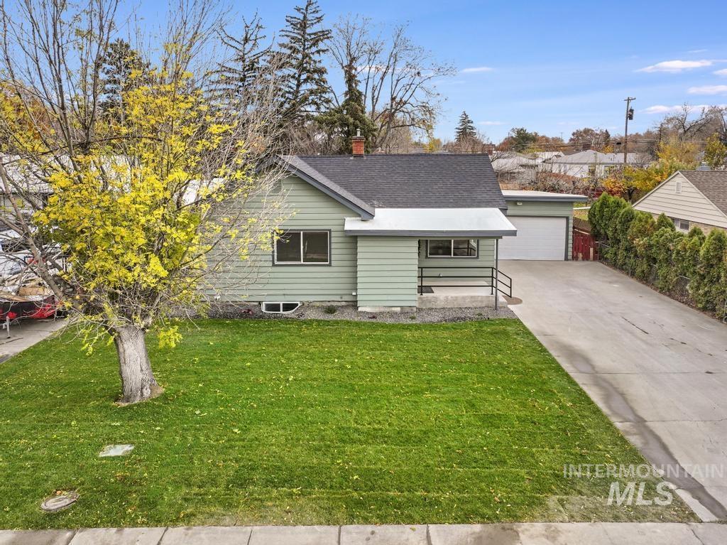 View of front of property with a front yard, a shingled roof, and a detached garage