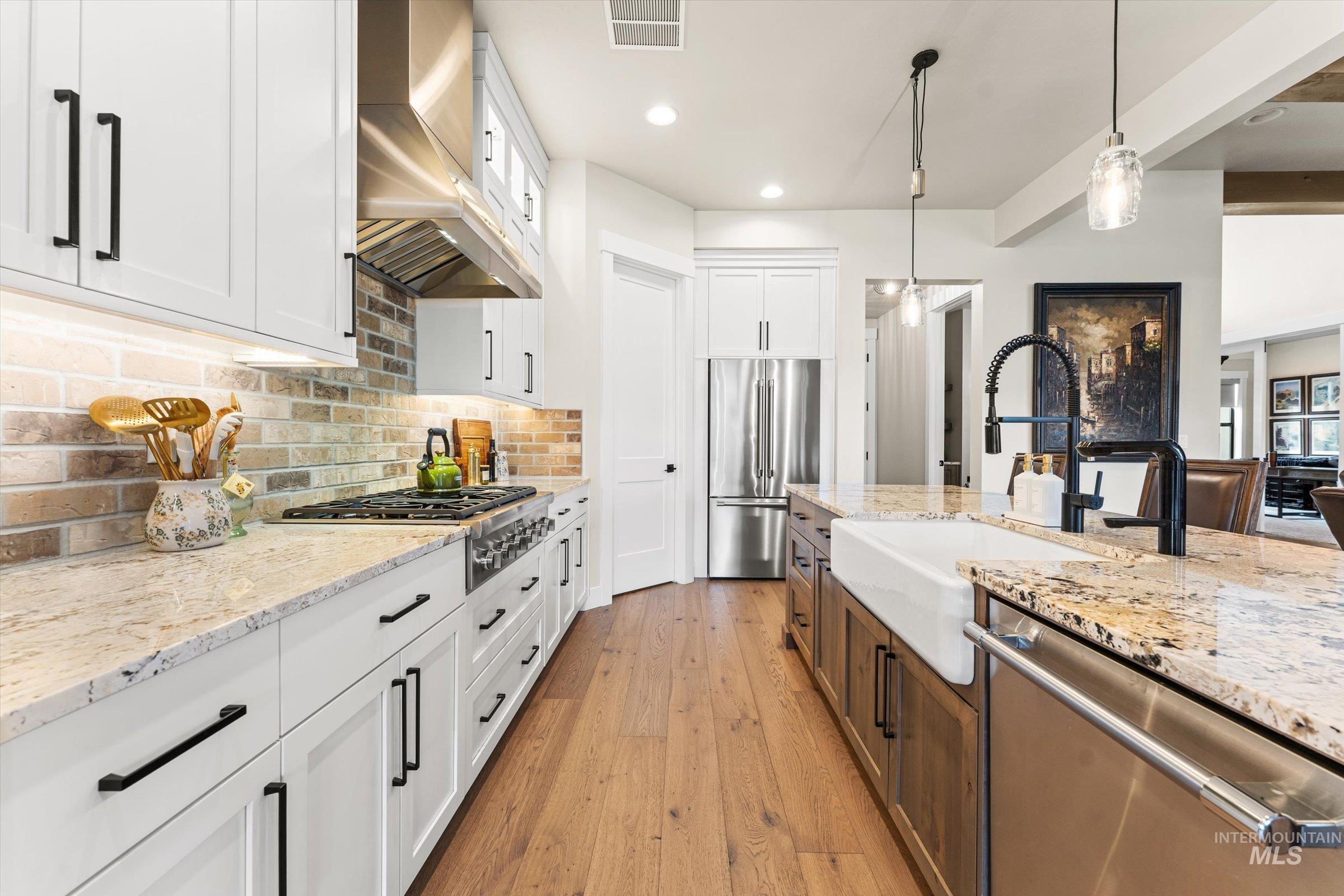 Two tone kitchen featuring two tone cabinets, stainless steel appliances, light wood finished floors, light stone countertops, and decorative backsplash
