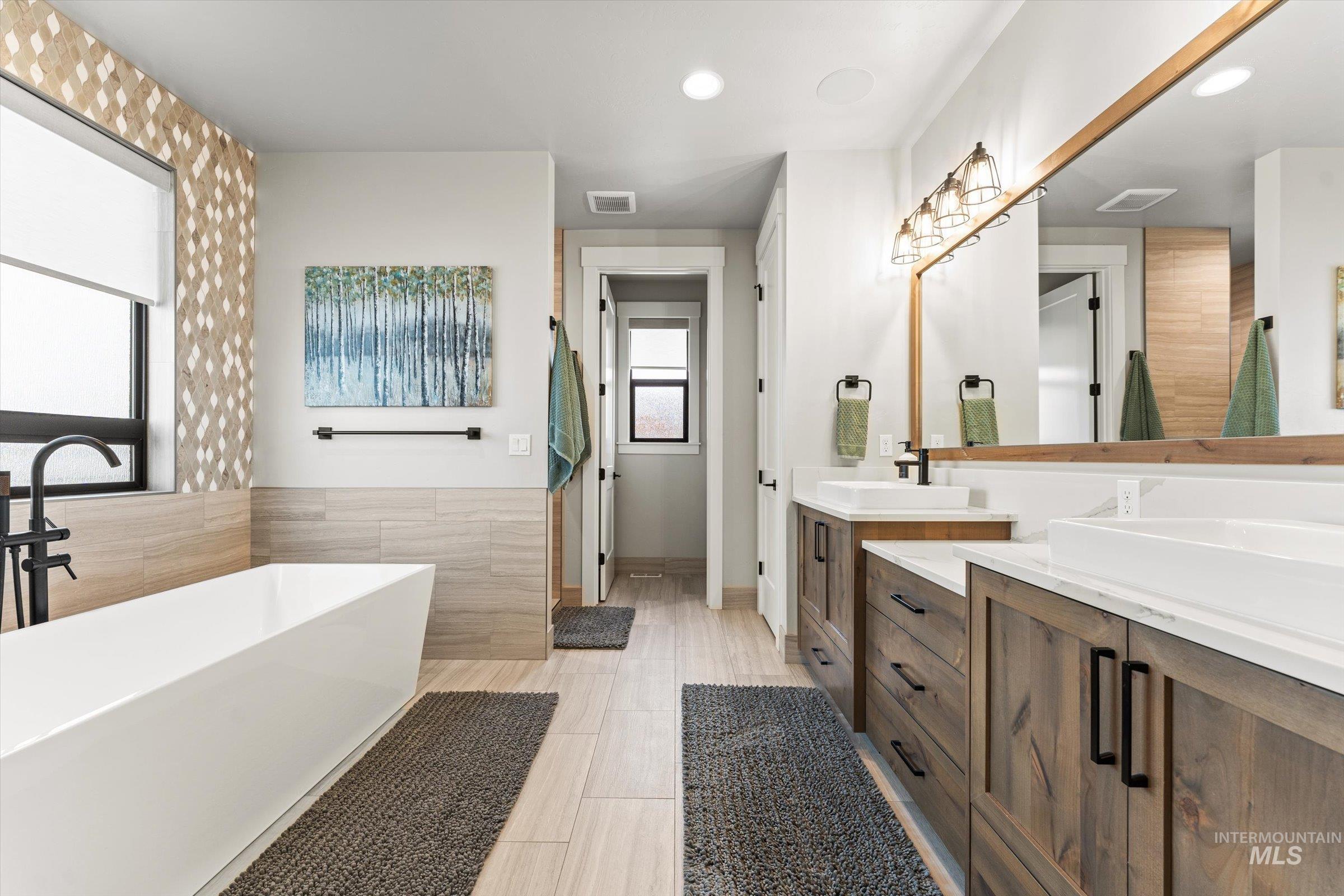 Bathroom with double vanity, a freestanding bath, recessed lighting, tile walls, and a wainscoted wall