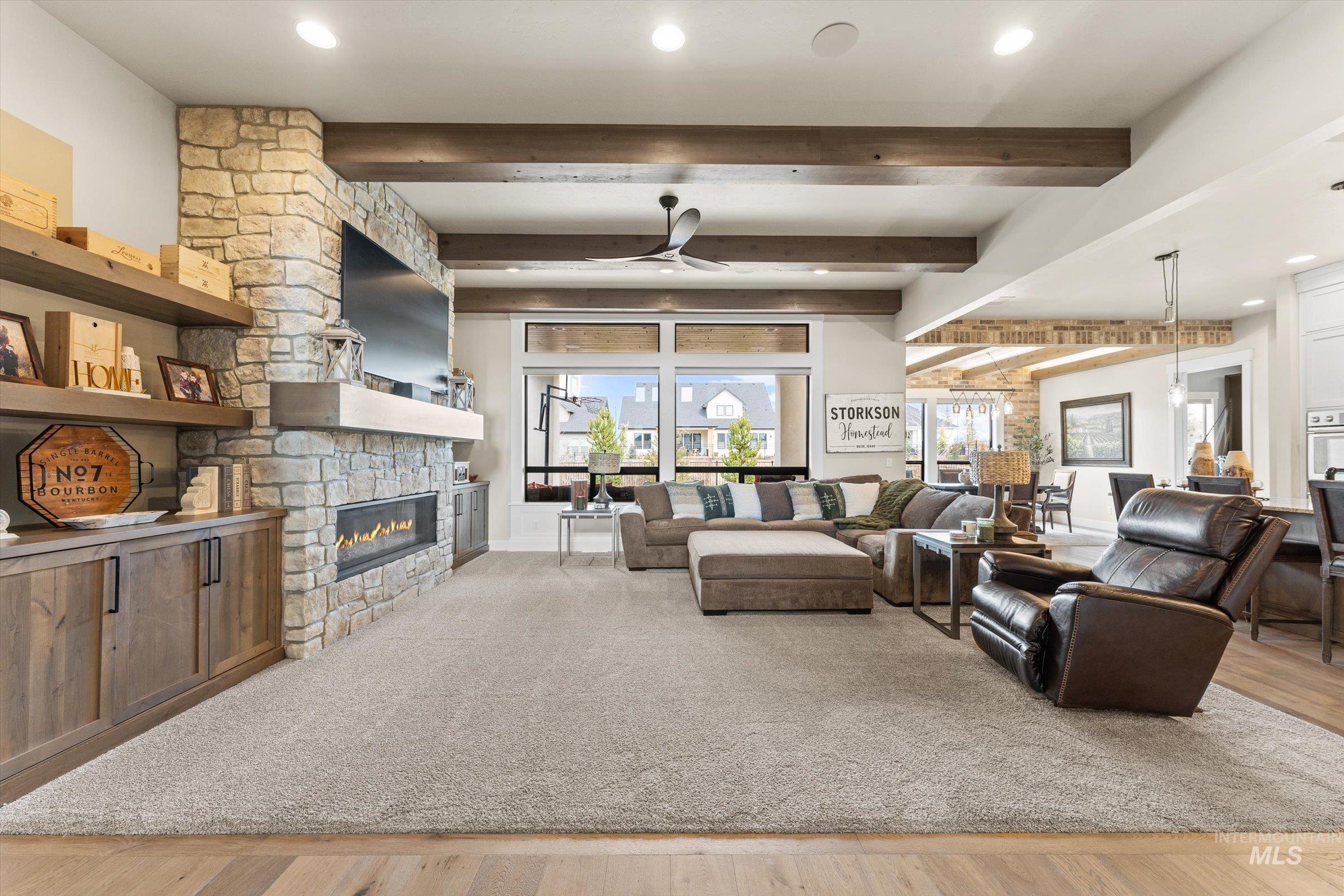 Living room featuring beam ceiling, ceiling fan, light wood-style floors, a fireplace, and recessed lighting