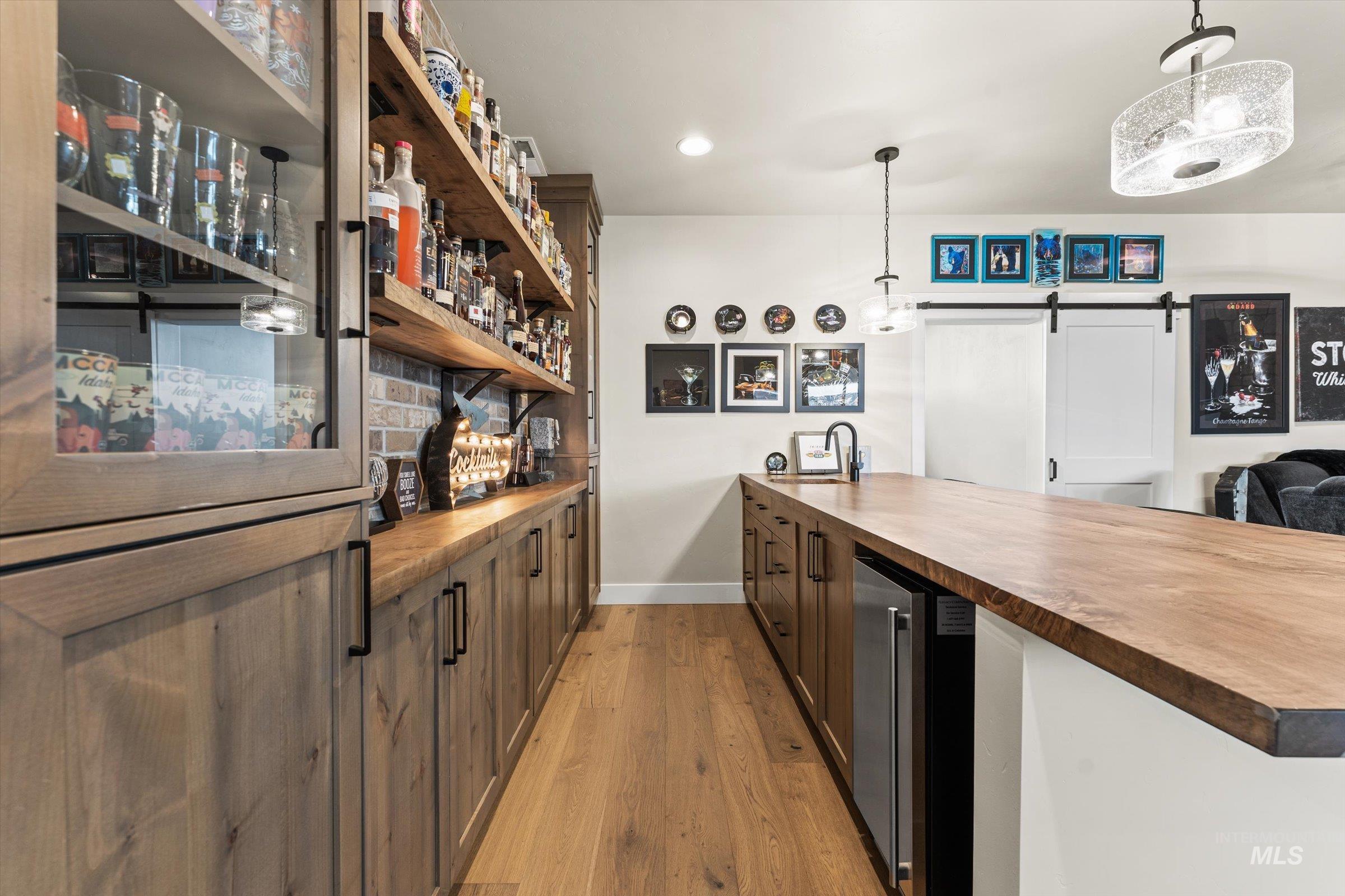 Indoor wet bar featuring butcher block counters, a barn door, light wood-style flooring, and pendant lighting