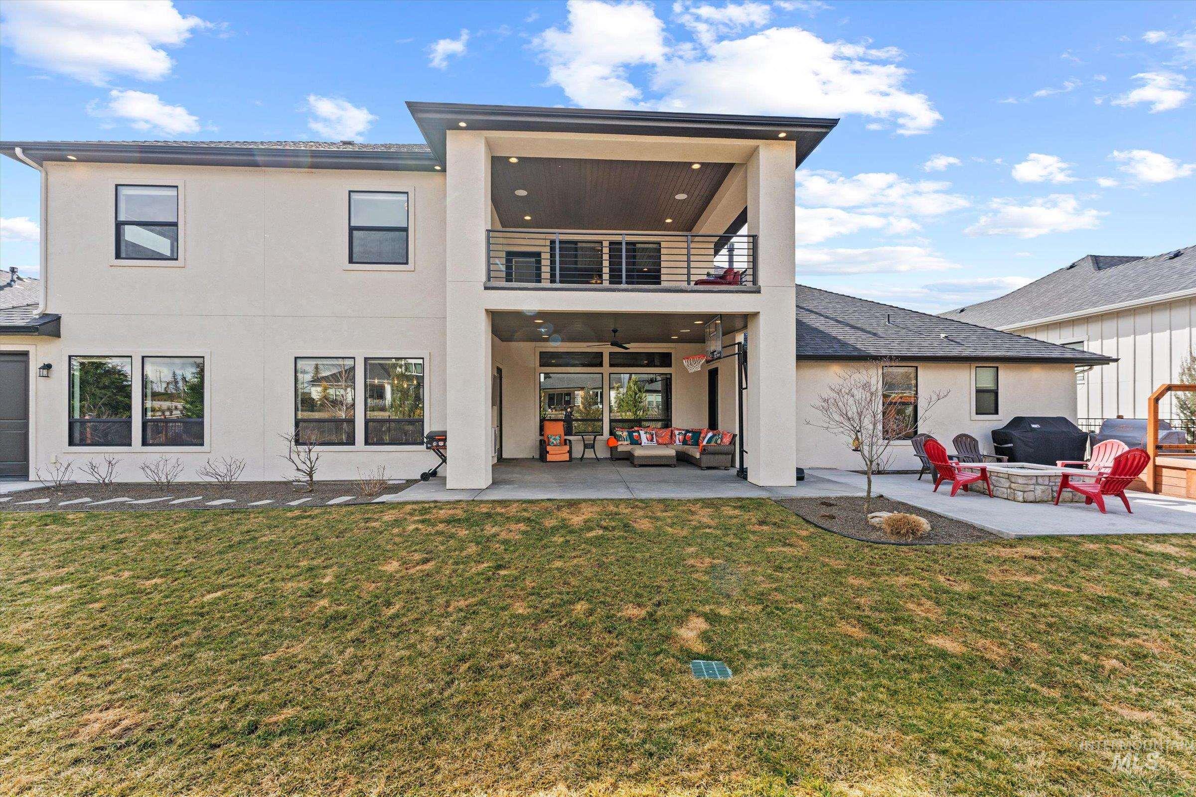 Rear view of house with a patio, stucco siding, a balcony, and a lawn