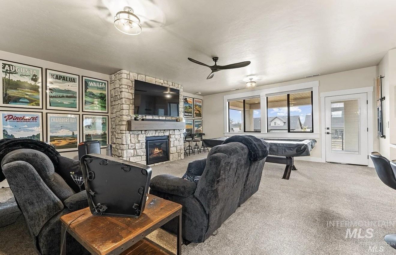 Living room featuring a stone fireplace, carpet, and ceiling fan