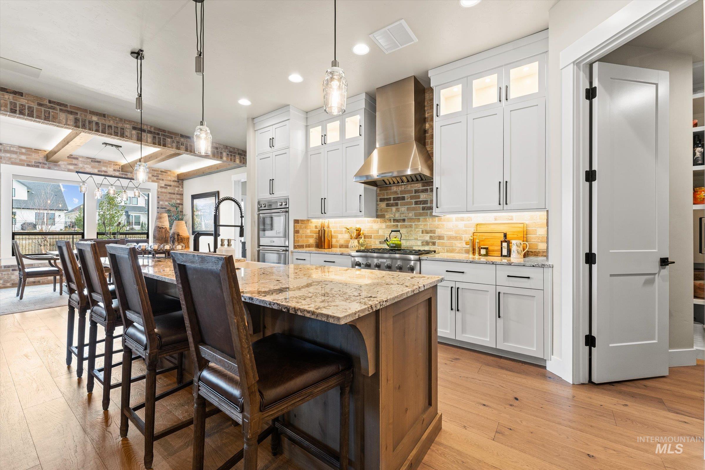 Two tone kitchen with two tone color scheme, light stone countertops, glass insert cabinets, a center island with sink, and a kitchen breakfast bar