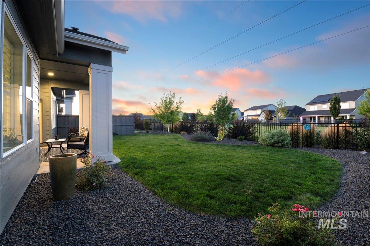 Yard at dusk with a fenced backyard, a residential view, and a patio area
