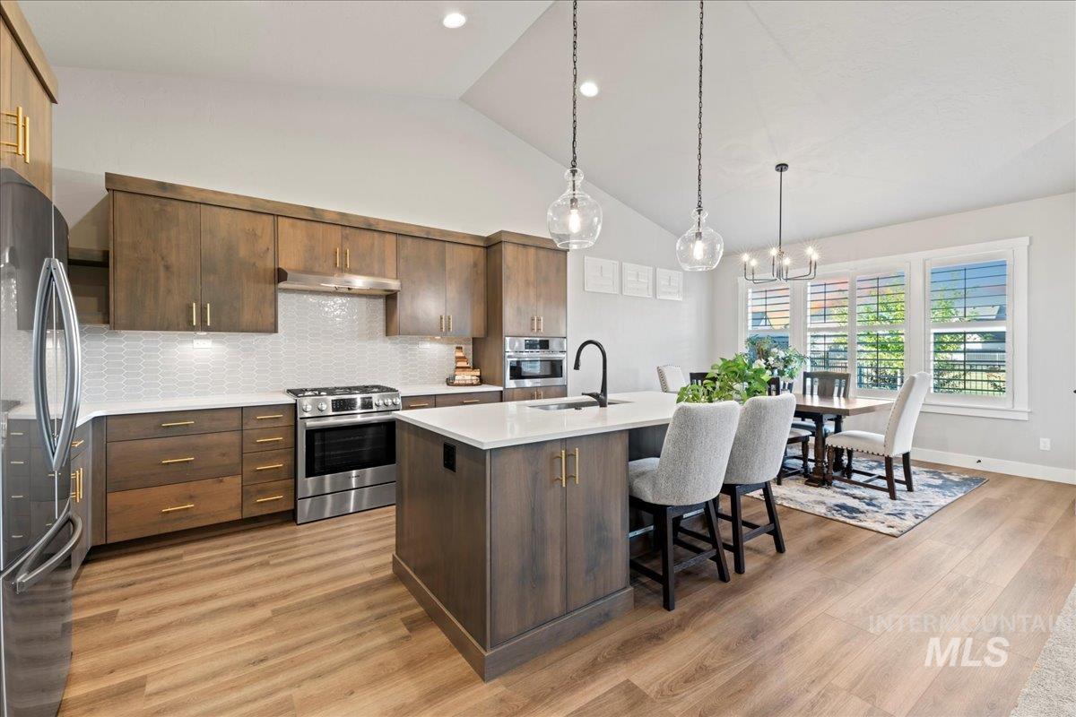 Kitchen featuring tasteful backsplash, stainless steel appliances, hanging light fixtures, light stone countertops, and light wood-type flooring