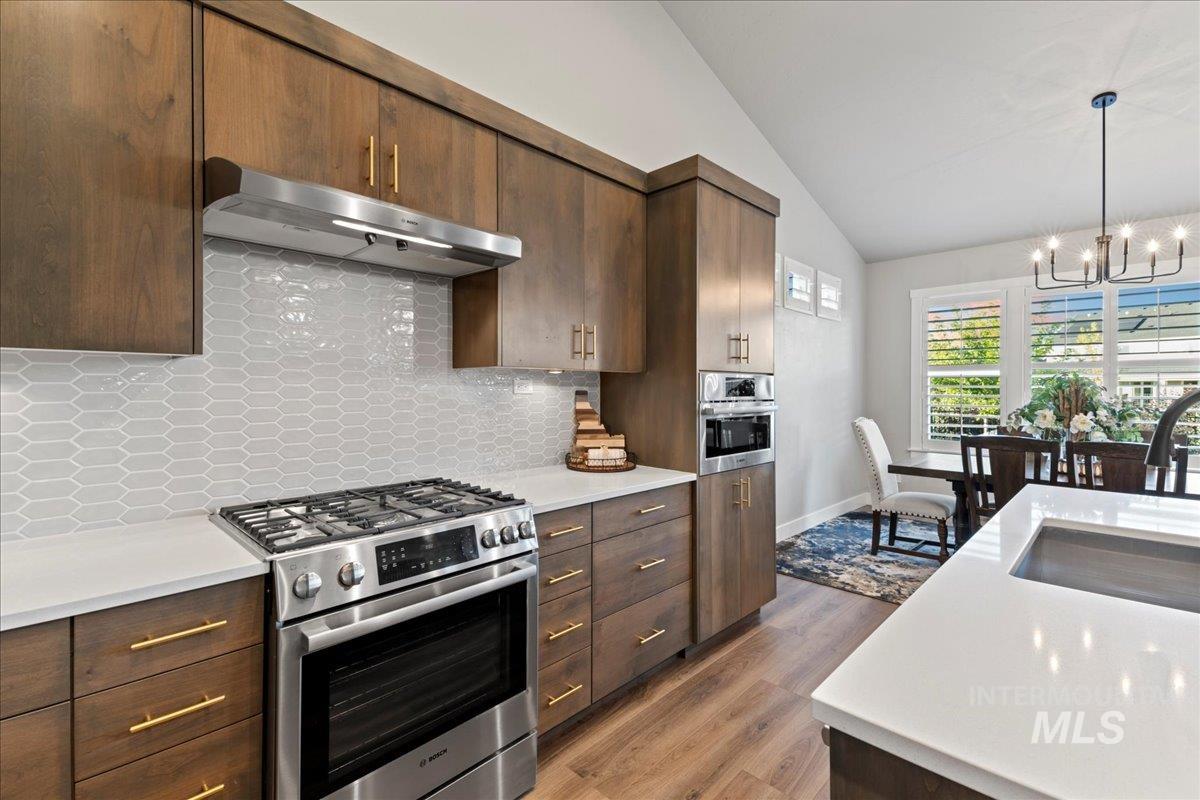 Kitchen with gas range, range hood, dark wood finished floors, tasteful backsplash, and dark brown cabinets