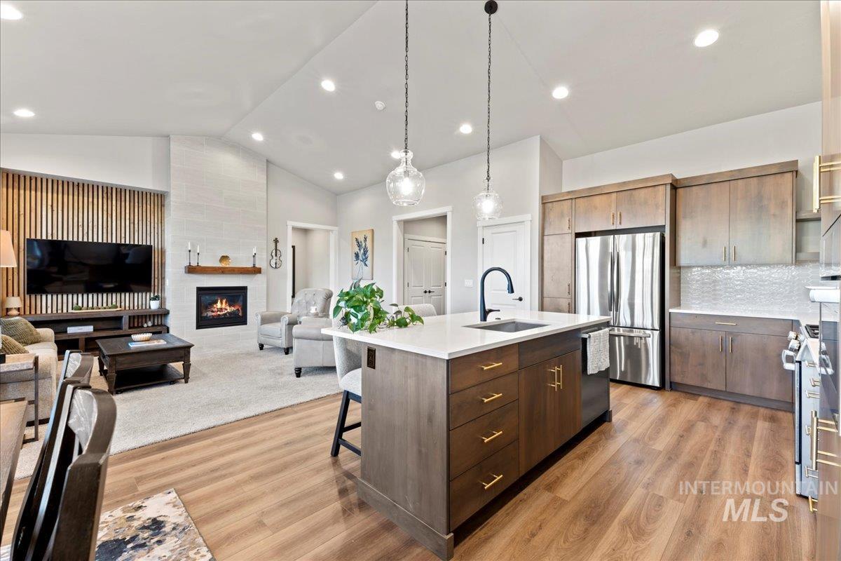 Kitchen with hanging light fixtures, open floor plan, a fireplace, appliances with stainless steel finishes, and a kitchen bar