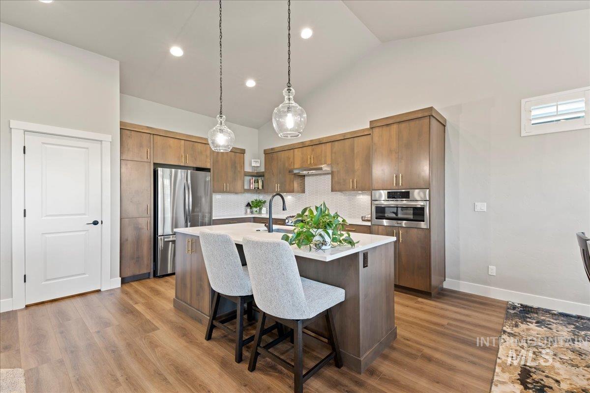 Kitchen with lofted ceiling, pendant lighting, a breakfast bar area, stainless steel appliances, and an island with sink